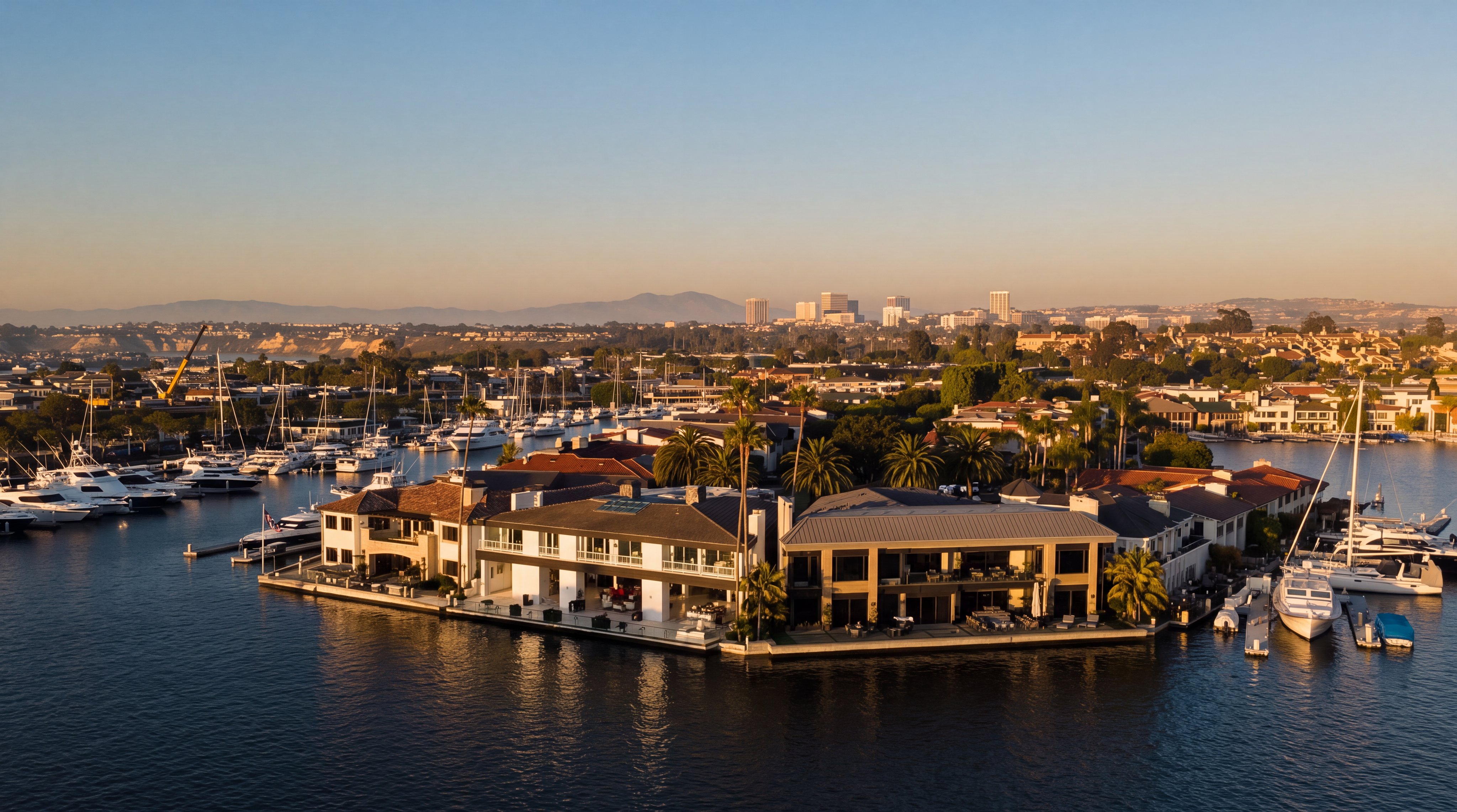 This high-angle aerial view captures a luxurious waterfront estate situated on a calm harbor, surrounded by numerous private boat slips and yachts. The property features a multi-level residence with expansive balconies and a private dock, showcasing a prime location for coastal living. The clear blue sky and the surrounding marina create a serene and upscale atmosphere, highlighting the property's exclusive access to the water.