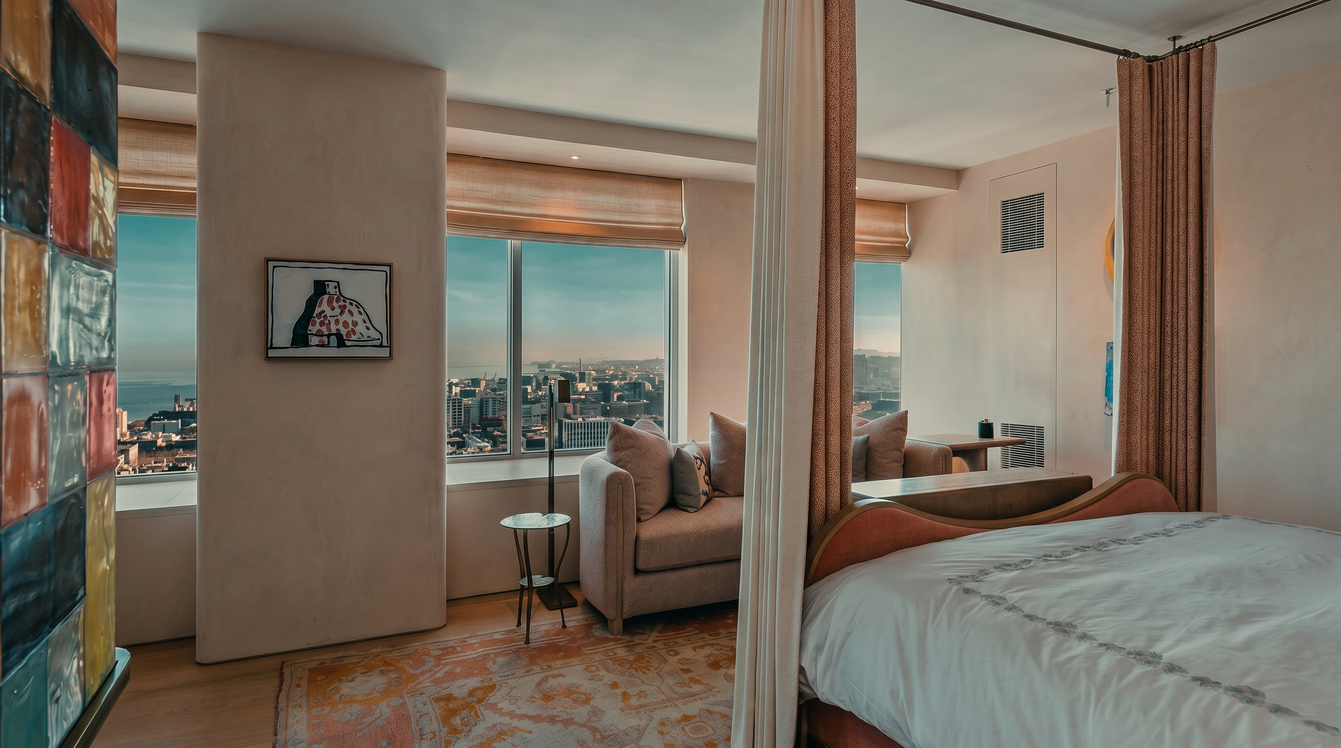 This primary bedroom features a canopy bed with soft pink accents and a white duvet, positioned to take advantage of the expansive city views through large windows. A cozy seating area with a plush armchair is tucked near the window, while a patterned area rug adds warmth to the light wood flooring. The room is decorated with a unique, colorful glass art installation on the left wall, creating a sophisticated and airy atmosphere.