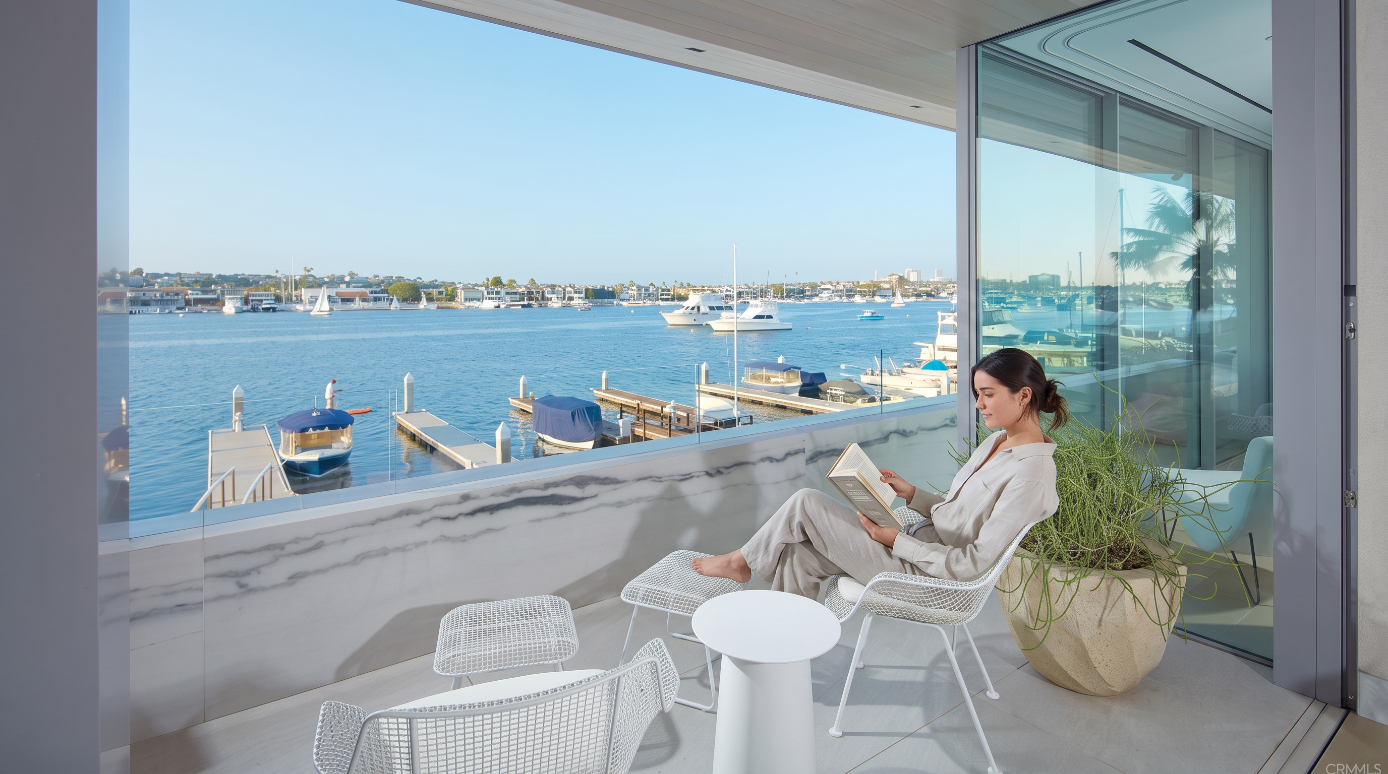 This luxurious balcony offers a serene, panoramic view of a harbor filled with boats and yachts, creating an elevated waterfront living experience. The space is elegantly furnished with contemporary white wire-frame outdoor furniture and accented by a stylish marble-patterned balustrade and a large, textured planter. The seamless indoor-outdoor integration is highlighted by floor-to-ceiling glass, providing a bright, tranquil setting for relaxation.