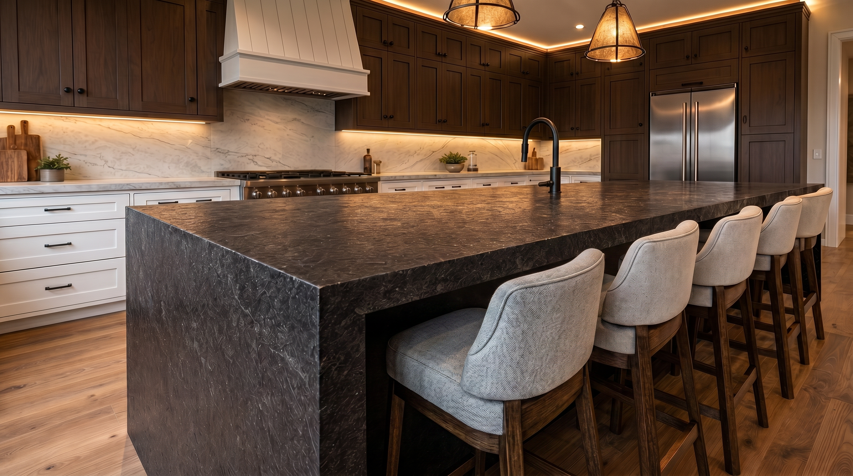 This sophisticated kitchen features dark wood cabinetry, a striking black textured stone island, and a matching range hood. The space is accented by warm under-cabinet lighting and minimalist pendant lamps, creating an elegant and modern atmosphere. Four upholstered bar stools provide seating at the island, making it an ideal gathering space.