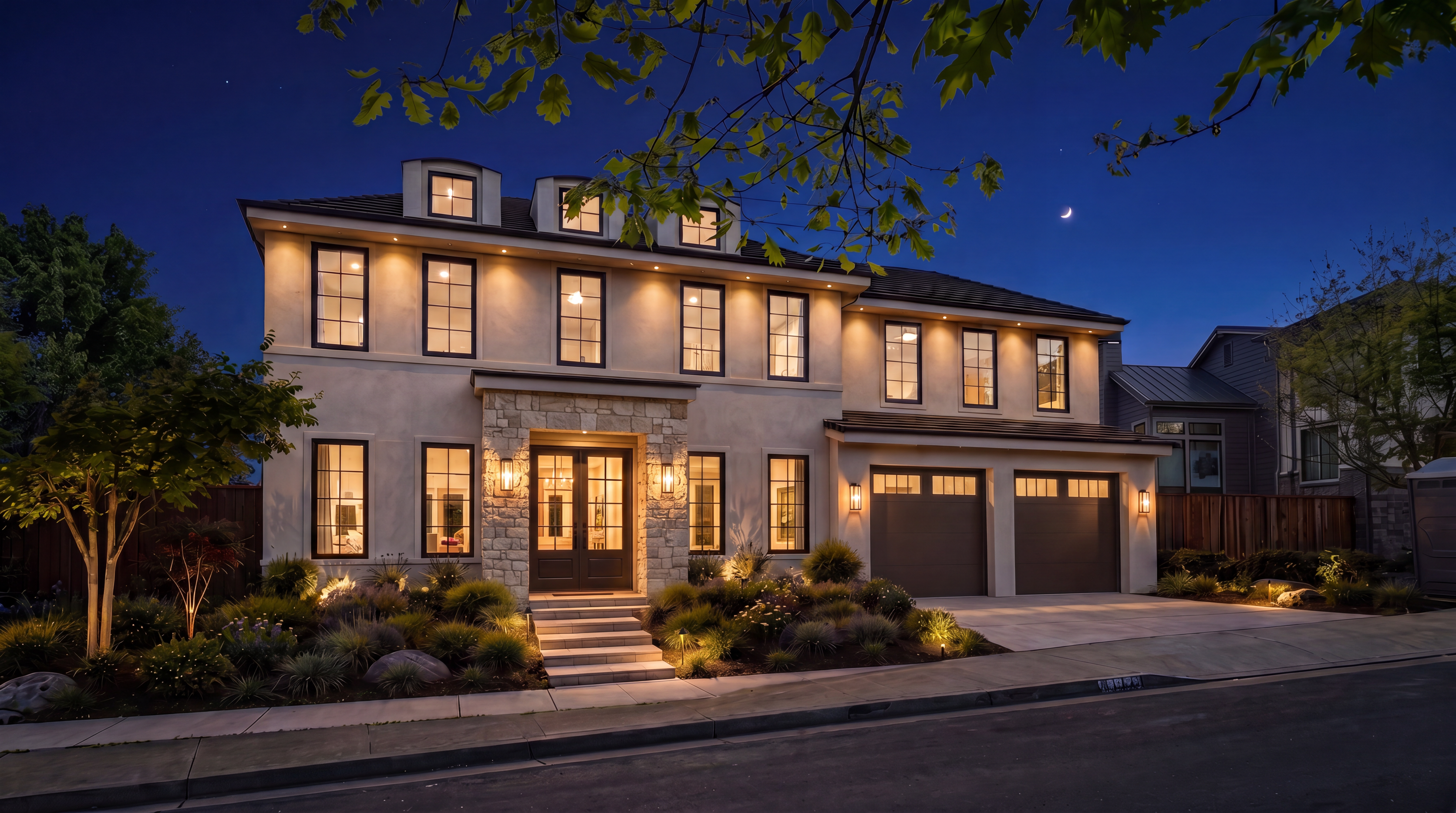 This elegant multi-story home features a sophisticated blend of light stucco and natural stone accents, creating a timeless and inviting curb appeal. The exterior is beautifully illuminated by warm recessed and wall-mounted lighting, highlighting the structured landscaping and formal entryway. With its symmetrical windows, attached two-car garage, and neatly paved driveway, the property projects a high-end, well-maintained aesthetic perfect for a luxury real estate listing.