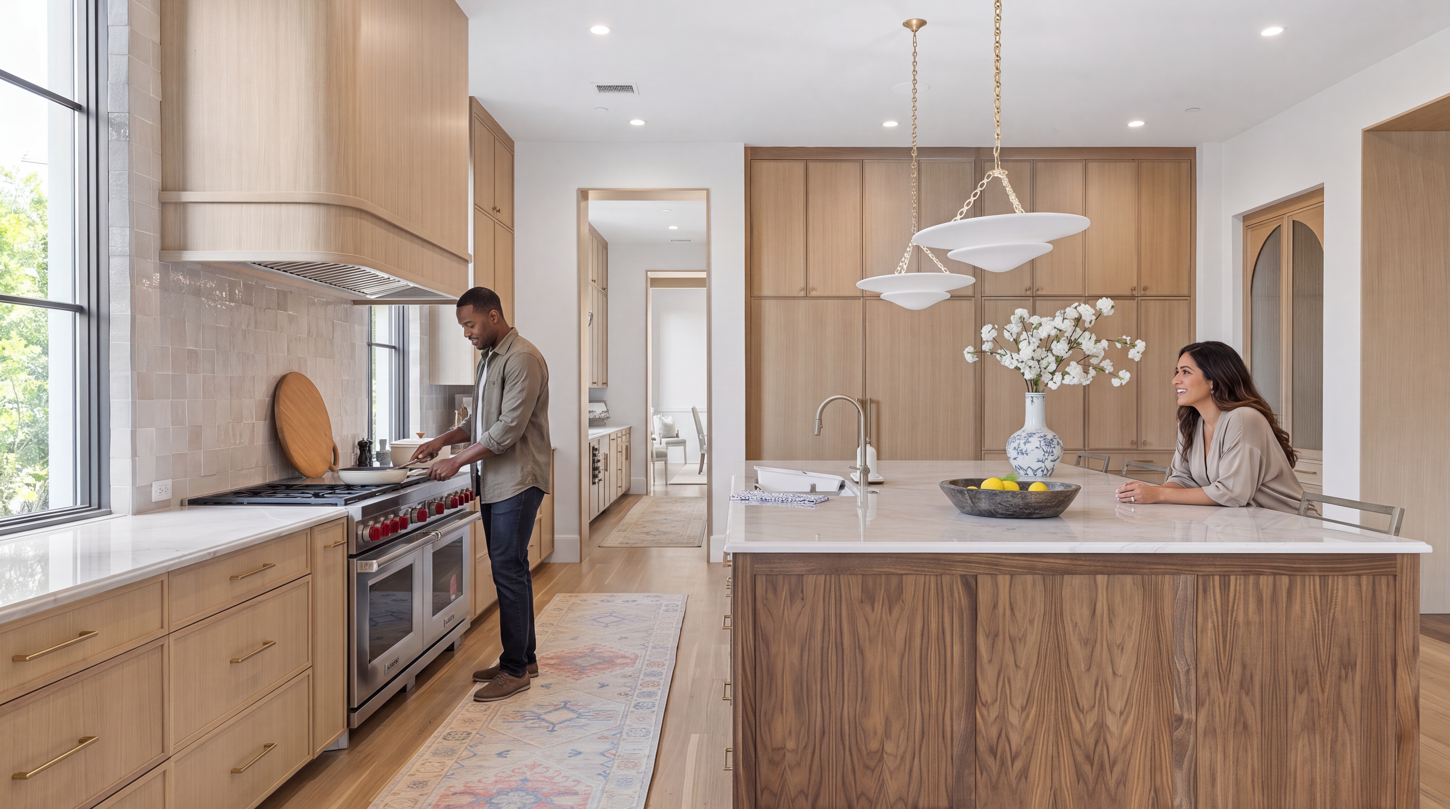This sophisticated kitchen showcases a high-end design with light oak custom cabinetry, marble countertops, and a prominent wood-paneled center island. The space features premium stainless steel range appliances, elegant pendant lighting, and a cohesive blend of organic textures and clean lines. An open-concept layout creates a warm and inviting atmosphere, perfect for both culinary activity and social interaction.