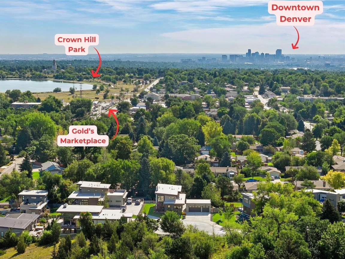 This high-angle aerial view captures a modern residential property nestled within a lush, tree-filled neighborhood. The perspective highlights the home's contemporary architecture and its proximity to local landmarks, including Crown Hill Park and the distant Denver skyline. The surrounding landscape is characterized by mature greenery and suburban streets, providing a clear sense of the property's location and setting.
