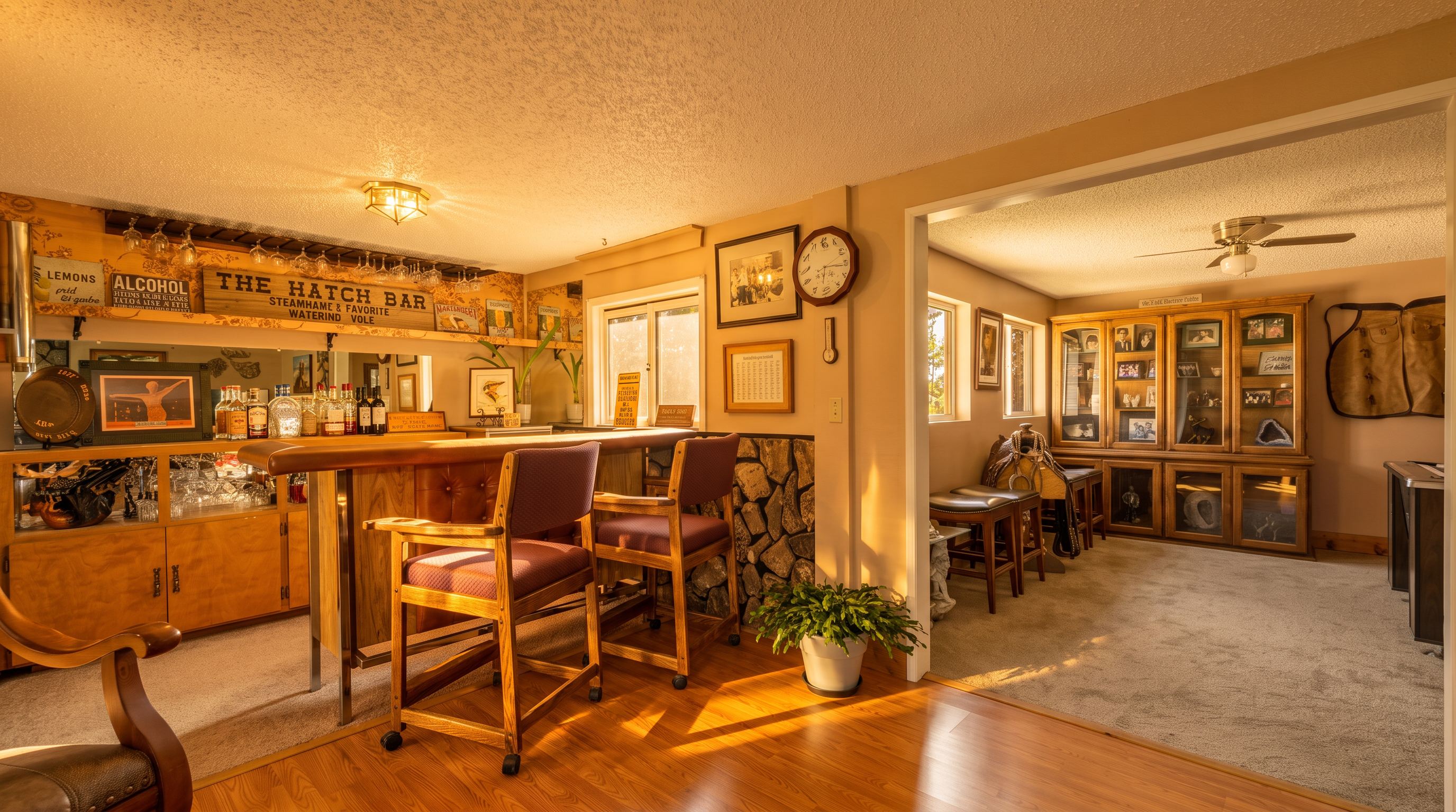 This basement space features a dedicated home bar area with a wooden counter, two bar stools, and a mirrored back wall with shelving for glassware and spirits. Adjacent to the bar is a carpeted lounge area furnished with a large wooden display cabinet and western-themed decor, including a saddle. The room combines wood-look flooring in the bar area with neutral carpeting, creating a casual, rustic entertainment space.