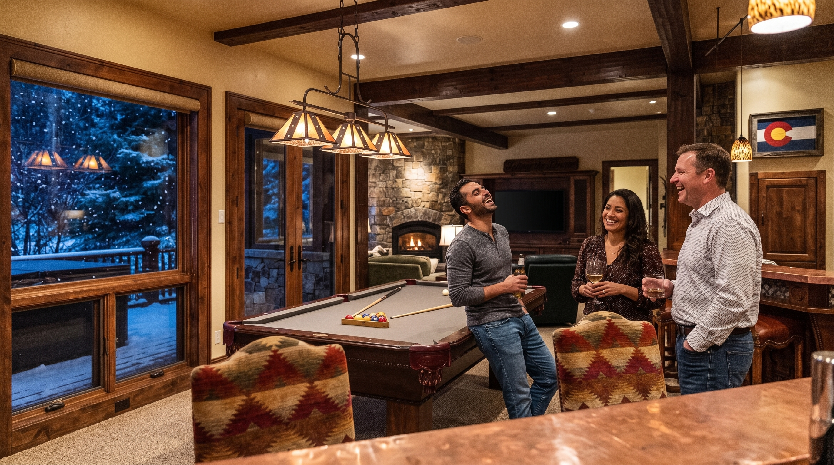 This cozy, rustic-style living room features a pool table as a central gathering point, perfect for entertaining. The space includes a stone fireplace, exposed wooden ceiling beams, and a large window providing scenic views of a snowy outdoor setting. The inviting atmosphere is enhanced by warm interior lighting and comfortable, patterned furniture, making it an ideal recreation space.
