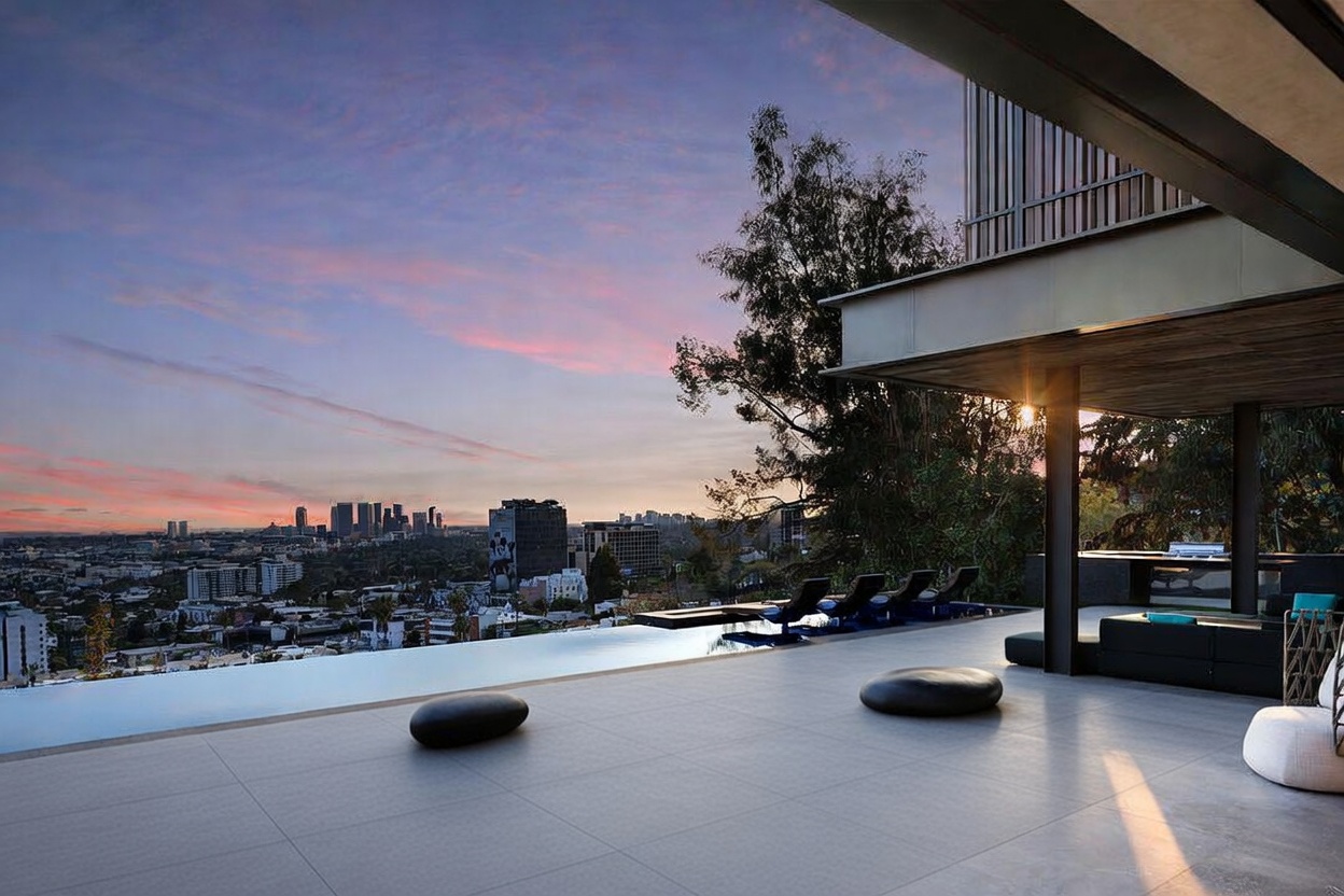 This stunning modern outdoor space features an infinity-edge pool that seamlessly blends into a panoramic sunset view of the city skyline. The area includes a manicured lawn with decorative stone accents, sleek lounge chairs, and a covered patio section, creating a sophisticated atmosphere for luxury entertaining. The architectural design emphasizes clean lines and an open-concept connection between the indoor living space and the expansive outdoor terrace.