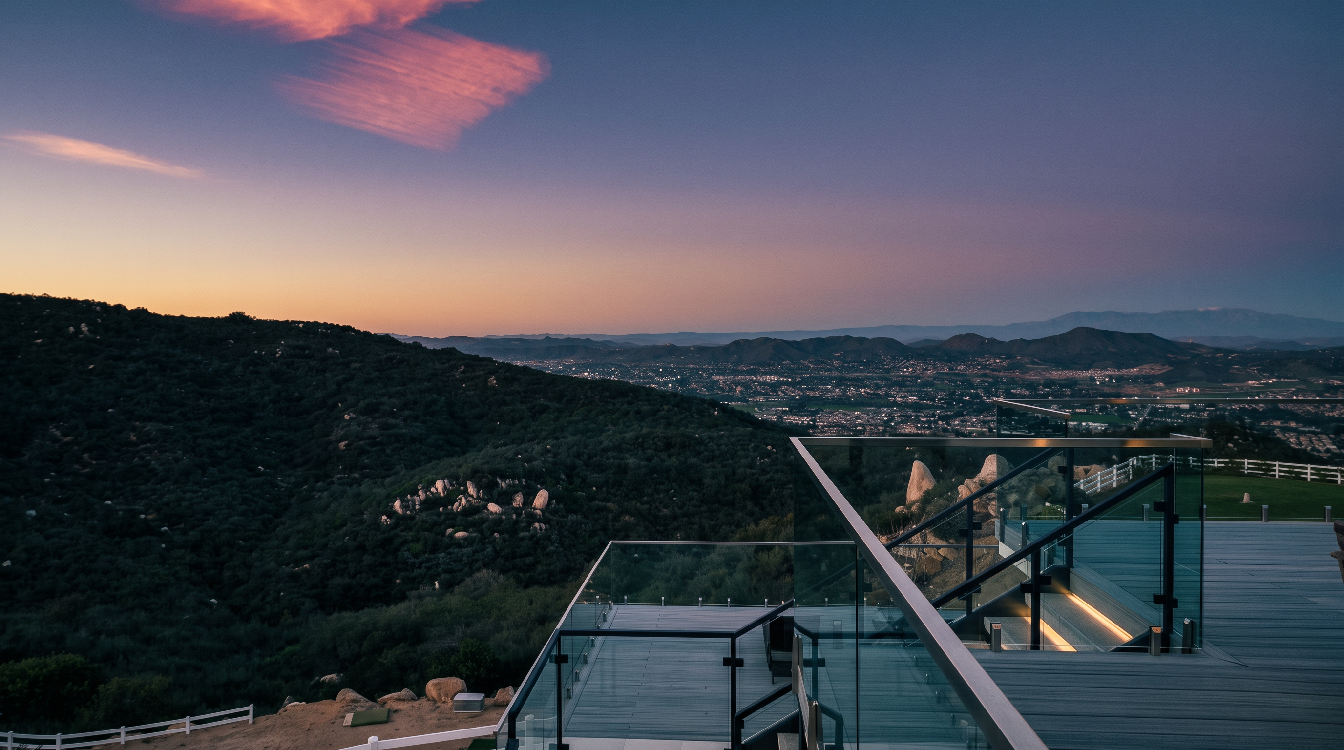 This stunning multi-level deck offers an expansive, unobstructed panoramic view of the valley and mountains under a vibrant sunset sky. The modern design features sleek glass railings and composite decking, creating a sophisticated outdoor living space ideal for entertaining. The setting emphasizes a luxurious lifestyle with a focus on indoor-outdoor connectivity and breathtaking scenery.