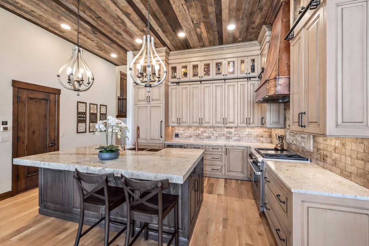 This spacious, rustic-inspired kitchen features a large central island with bar seating and light-toned stone countertops. The space is defined by a striking wood-plank ceiling, custom cabinetry with glass-front upper displays, and a prominent copper-toned range hood. A warm, inviting atmosphere is created by the combination of natural wood textures, stone backsplash, and elegant pendant lighting.
