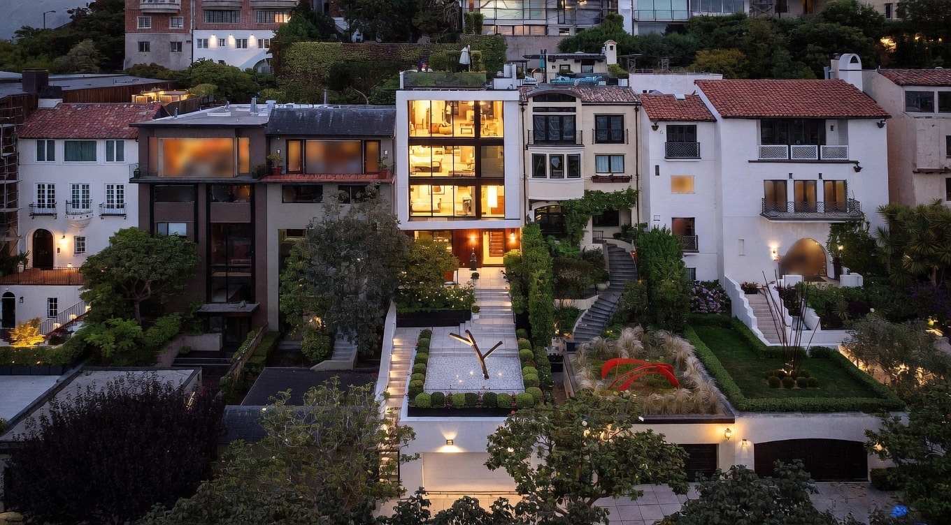 This aerial perspective captures a row of upscale, multi-story residences in a dense urban setting, highlighting a central modern home with a striking glass-fronted facade. The property features a tiered landscape design with a sculptural art piece, manicured greenery, and a stone staircase leading to the main entrance. The composition emphasizes the contrast between the contemporary architecture and the surrounding traditional homes, all illuminated by warm evening lighting.
