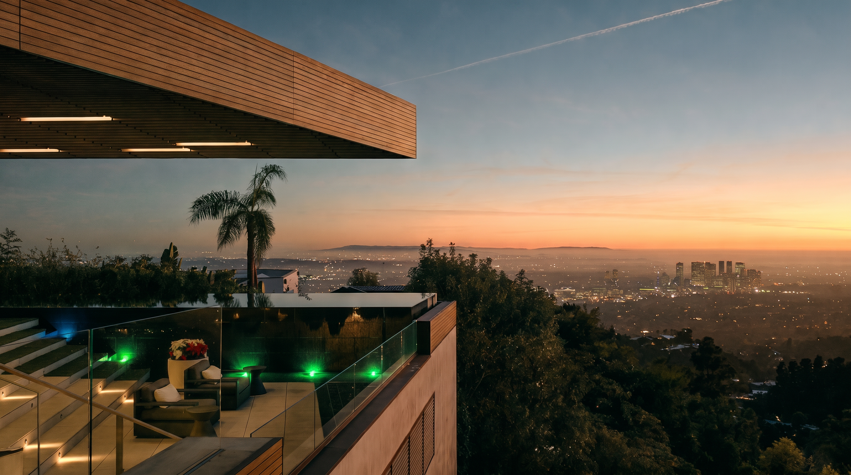 This stunning architectural balcony offers a panoramic, cinematic view of the Los Angeles city skyline at dusk. The space features modern, clean lines with warm wood-paneled ceilings, integrated lighting, and a glass railing that seamlessly connects the outdoor lounge area to the horizon. The combination of the elevated perspective, lush surrounding trees, and the glowing city lights creates a luxurious and serene atmosphere.