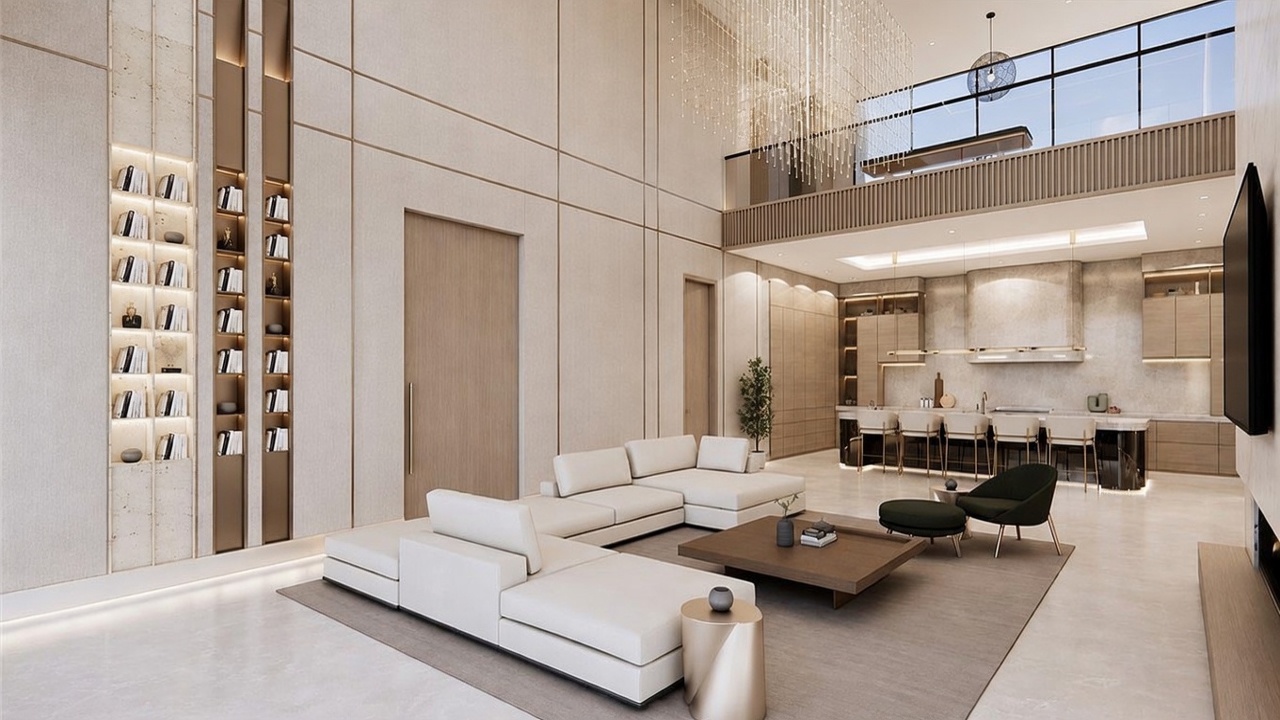 This expansive, double-height living area showcases a sophisticated contemporary design with a neutral color palette and clean lines. The space features a large, modular white sectional sofa, a low-profile wooden coffee table, and a sleek kitchen island with bar seating in the background. A dramatic, multi-tiered crystal chandelier hangs from the upper level, while a glass-railed mezzanine overlooks the main living area, creating an airy and open atmosphere.