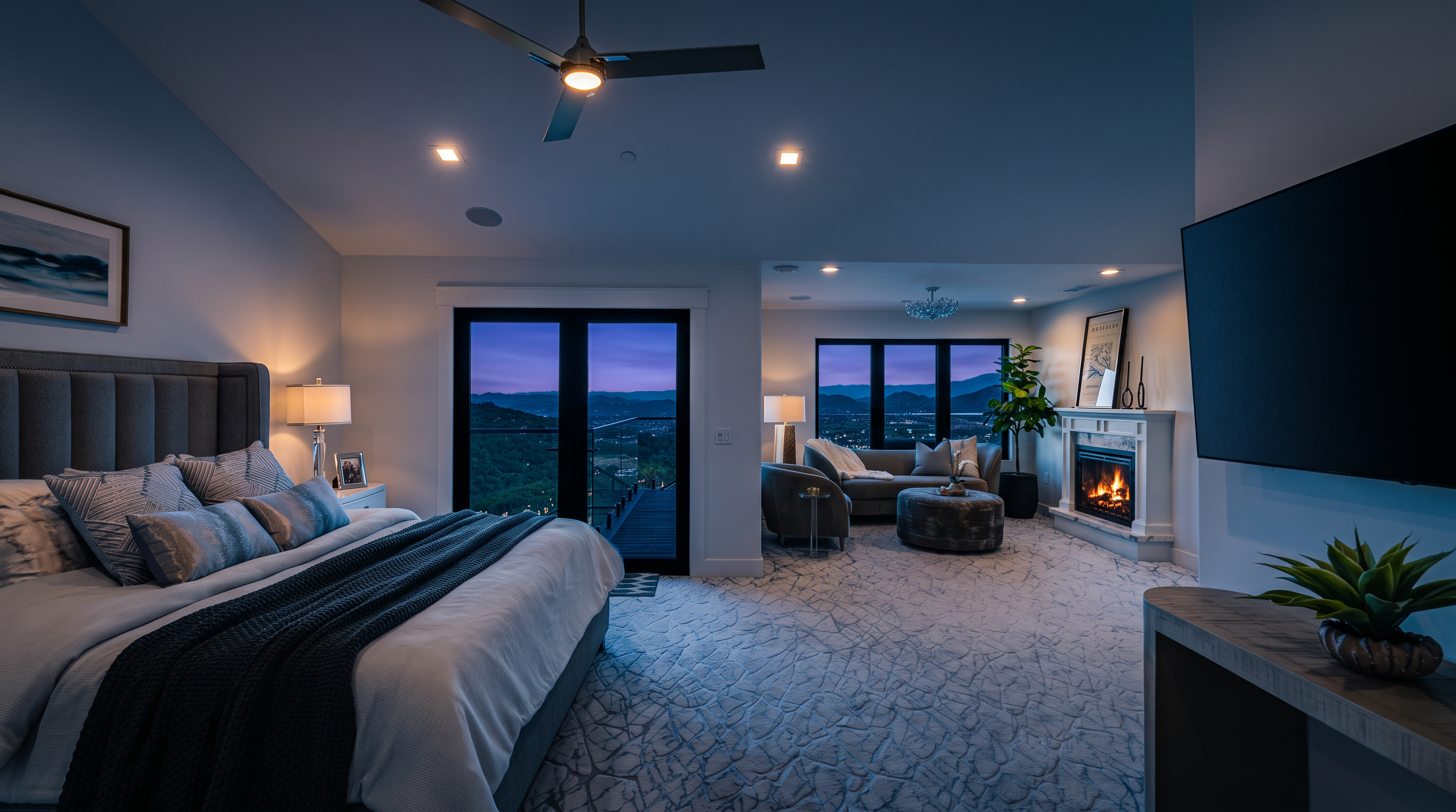 This luxurious primary bedroom features a spacious layout with a dedicated sitting area complete with a fireplace and stunning mountain views through expansive windows. The room is decorated in a sophisticated, neutral color palette with plush carpeting, a modern ceiling fan, and high-end furnishings, creating an elegant and tranquil retreat. Its open-concept design seamlessly blends the sleeping area with a comfortable lounge space, highlighting the property's premium architectural quality.