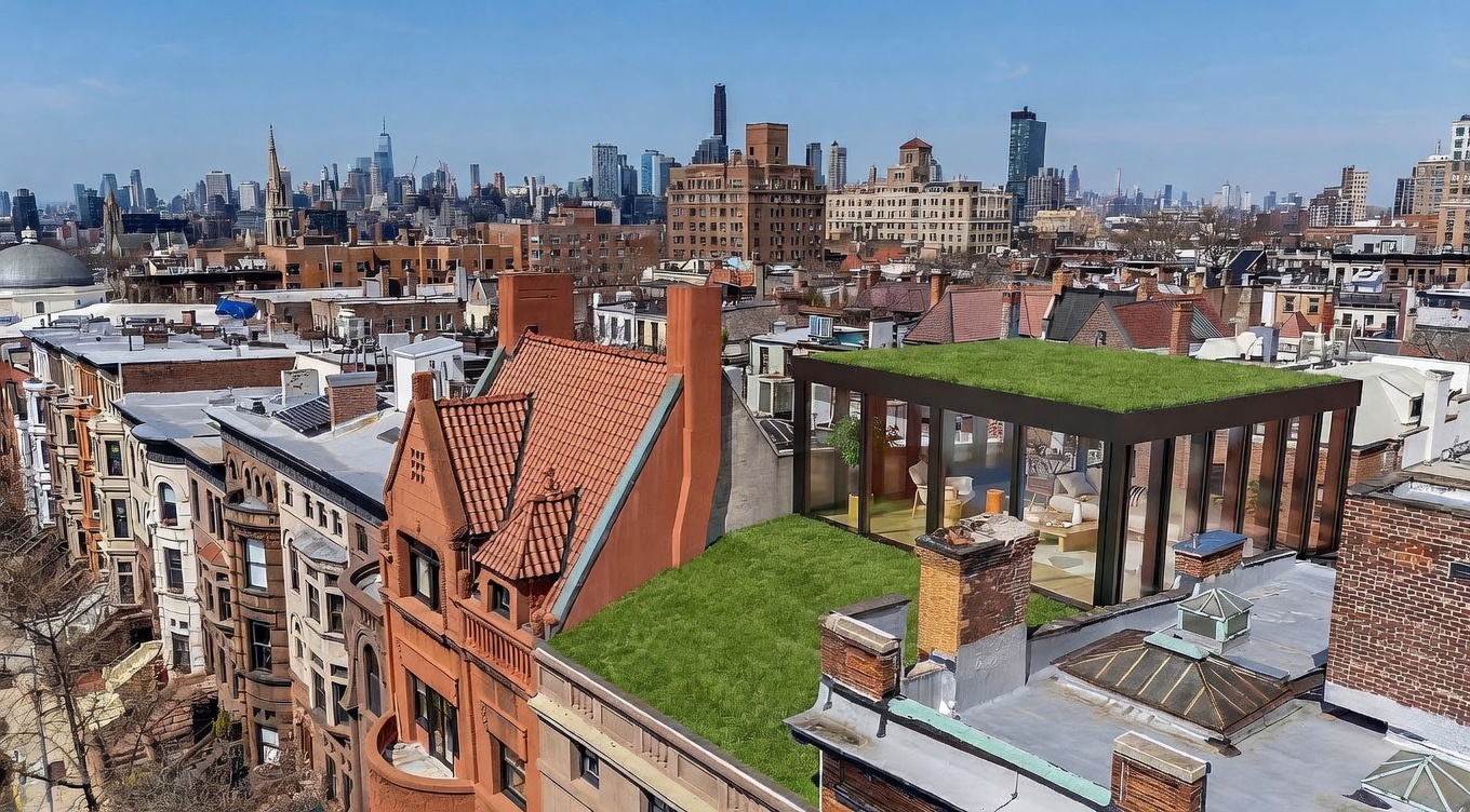 This high-angle aerial view showcases a sophisticated urban rooftop renovation featuring a lush green lawn and a modern glass-enclosed structure. The scene captures a blend of historic brownstone architecture with contemporary design elements, set against a sprawling city skyline. The perspective provides a cinematic overview of the property's unique outdoor living space and its prime location within the dense cityscape.
