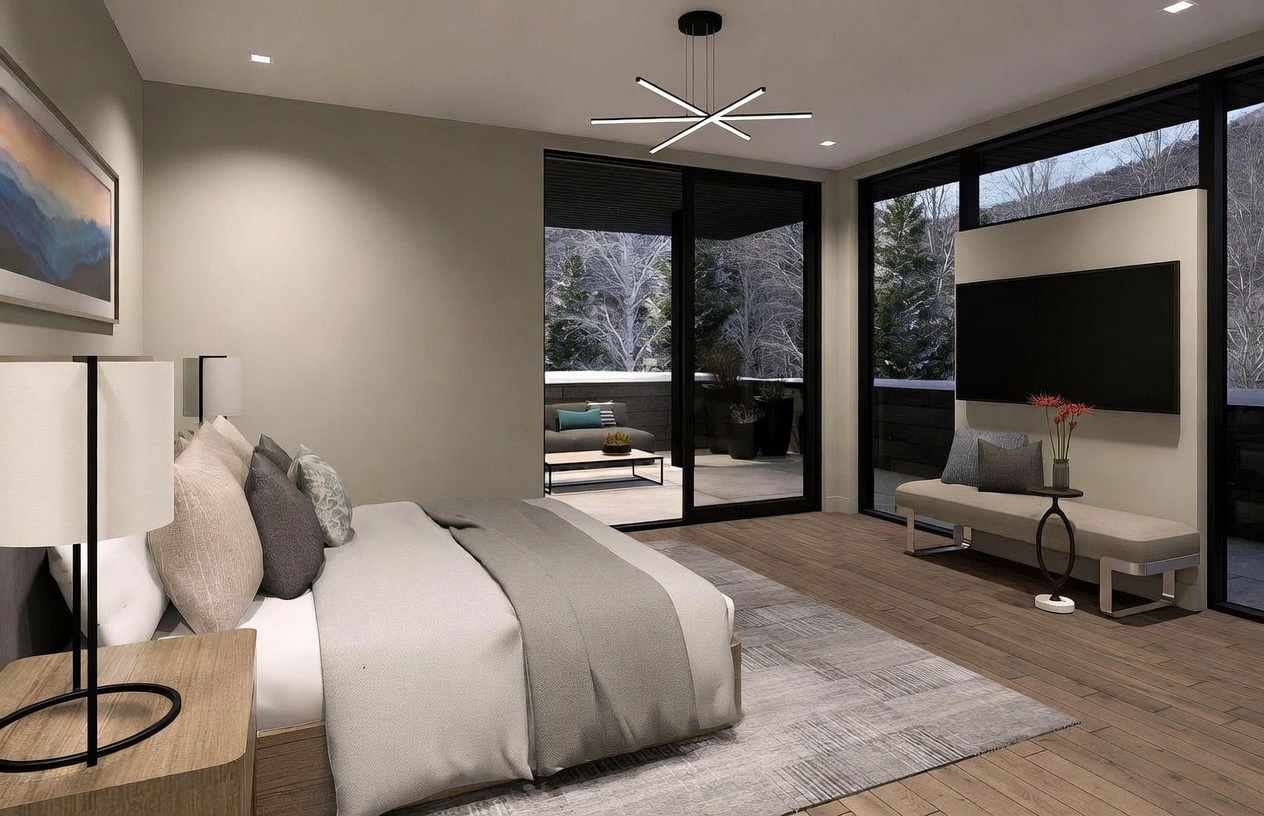 This contemporary primary bedroom features a neutral color palette, light wood flooring, and a large area rug. A wall-mounted television is positioned above a sleek bench, while large sliding glass doors provide access to a private balcony with views of a snowy landscape. The room is illuminated by a modern, geometric chandelier and soft ambient lighting, creating a serene and sophisticated atmosphere.