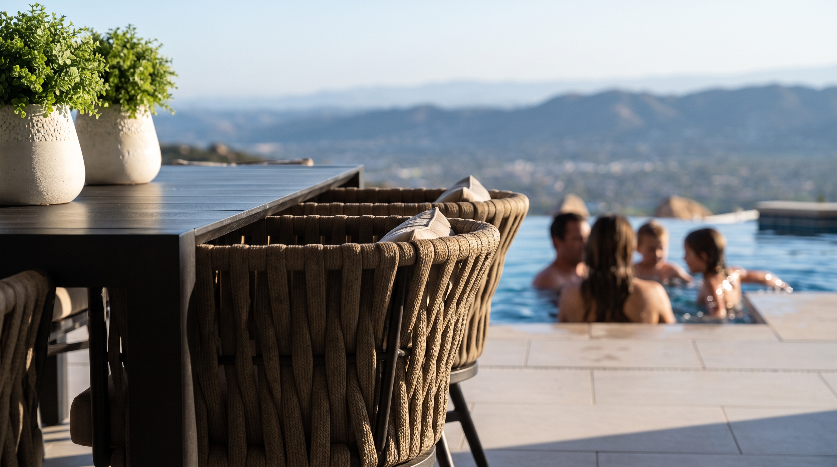 This stunning covered outdoor patio offers a seamless transition to a luxury infinity-edge pool with panoramic mountain and valley views. The space is elegantly appointed with a dark dining set, comfortable lounge furniture, and a stone fireplace, creating an ideal setting for high-end alfresco entertaining. The warm wood-paneled ceiling with recessed lighting and a sleek ceiling fan adds a sophisticated, resort-style atmosphere to this expansive outdoor living area.