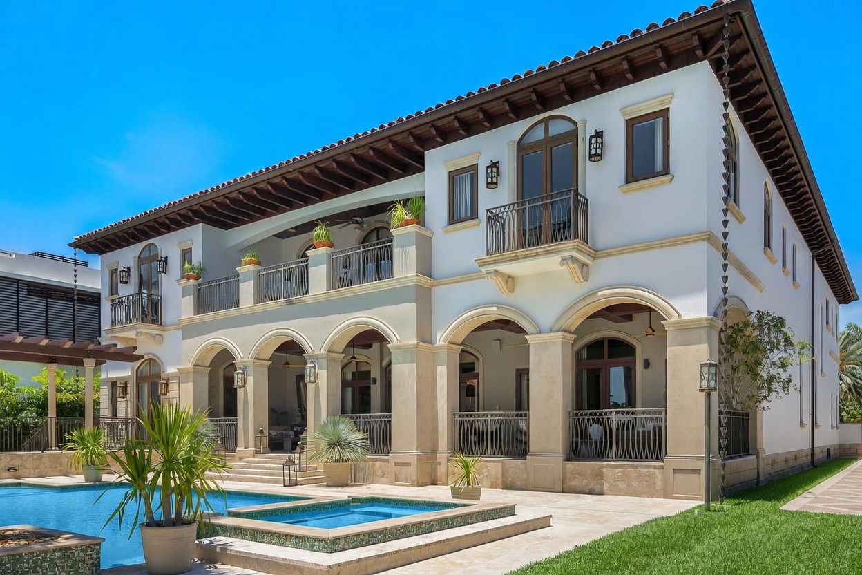 This stunning Mediterranean-style estate features a grand rear facade with elegant arched loggias, a spacious second-story balcony, and intricate architectural detailing. The property seamlessly integrates with a luxurious swimming pool and spa area, set against a backdrop of lush green landscaping. The perspective captures the sophisticated outdoor living space, emphasizing the home's impressive scale and high-end design.