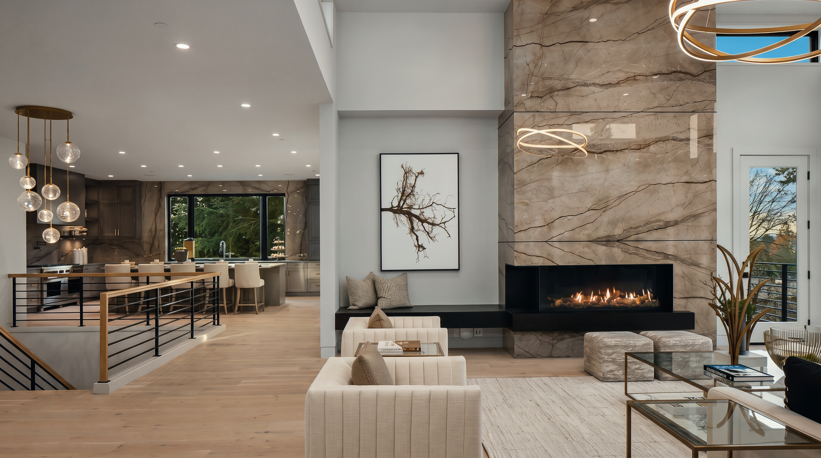 This open-concept living area features a striking stone-clad chimney breast that serves as a focal point, complemented by a modern linear fireplace and a built-in bench. The space flows seamlessly into a kitchen area with a large island and bar seating, all tied together by light wood flooring and a neutral color palette. The perspective captures the airy, high-ceilinged layout, emphasizing the sophisticated design and the connection between the living and dining spaces.