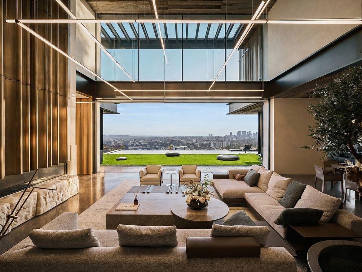This expansive, ultra-modern living room features a seamless indoor-outdoor transition through massive floor-to-ceiling glass walls that reveal a panoramic city view. The space is anchored by a large, low-profile sectional sofa and a central stone coffee table, complemented by a striking metallic fireplace wall and minimalist linear lighting fixtures. The overall aesthetic is one of sophisticated luxury, emphasizing open-concept design and high-end architectural finishes.