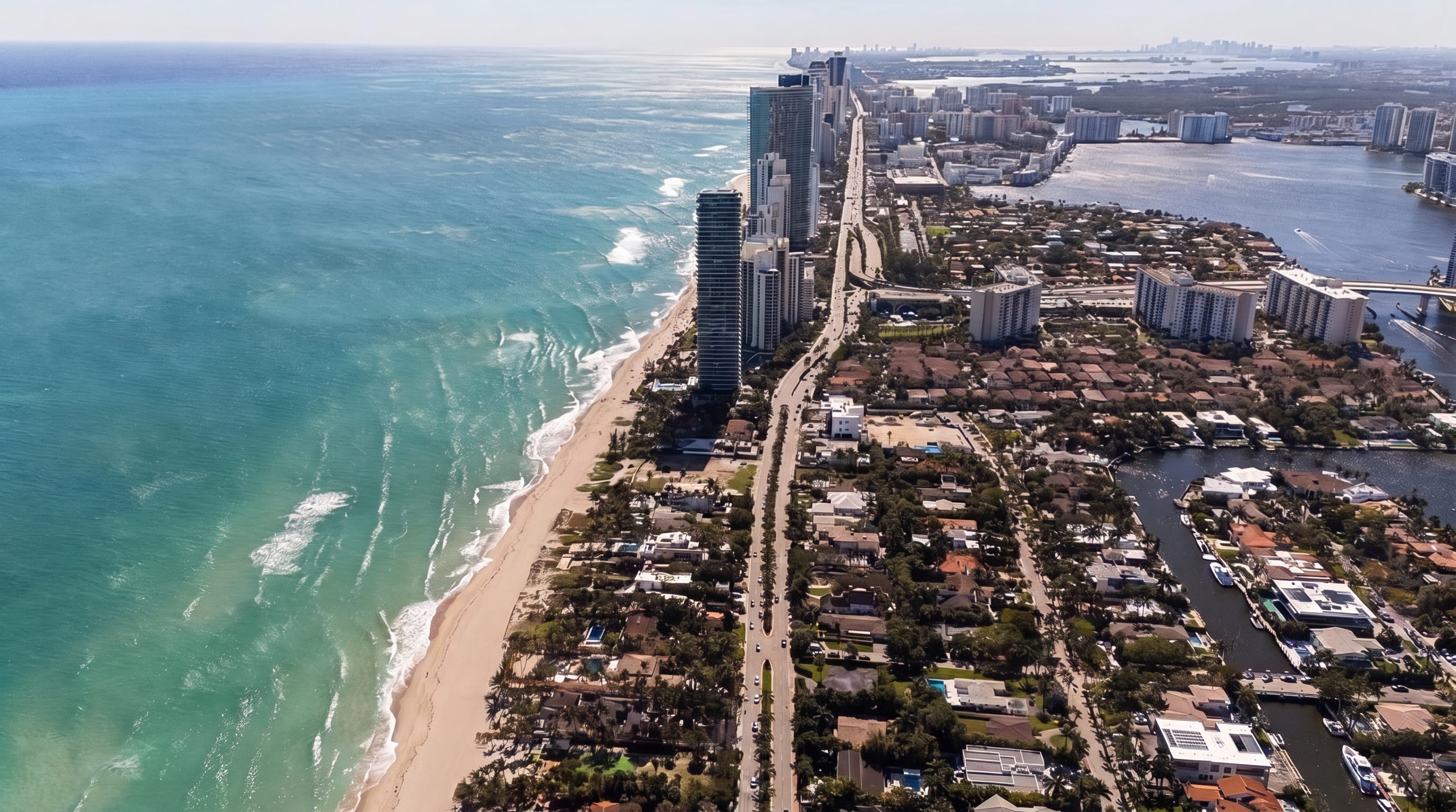 This high-altitude aerial view captures a prime stretch of Florida coastline, highlighting a specific beachfront property outlined in red. The perspective showcases the property's direct access to the sandy beach on one side and its proximity to a major coastal road and high-rise residential towers on the other. The surrounding area features a mix of lush tropical landscaping, residential homes, and a nearby waterway, emphasizing the desirable waterfront location.