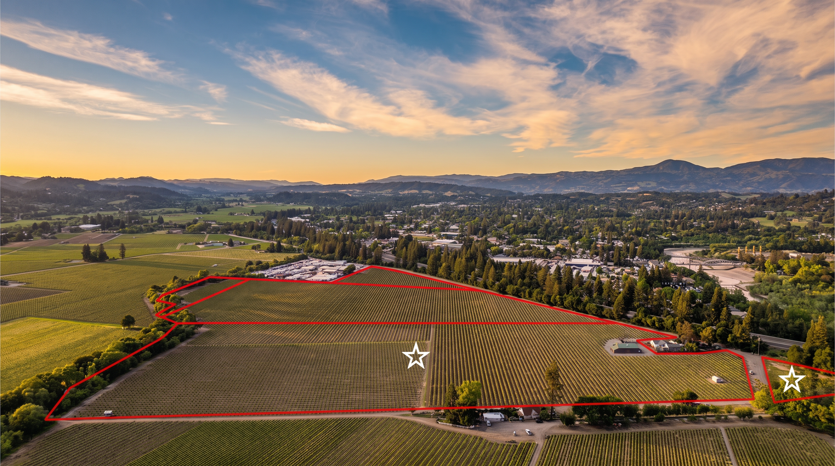 This is an expansive aerial view of a large vineyard property highlighted by a red boundary line. The landscape features extensive rows of grapevines, interspersed with small structures and a backdrop of lush trees and rolling hills in the distance. The property offers significant agricultural potential and serene countryside views.