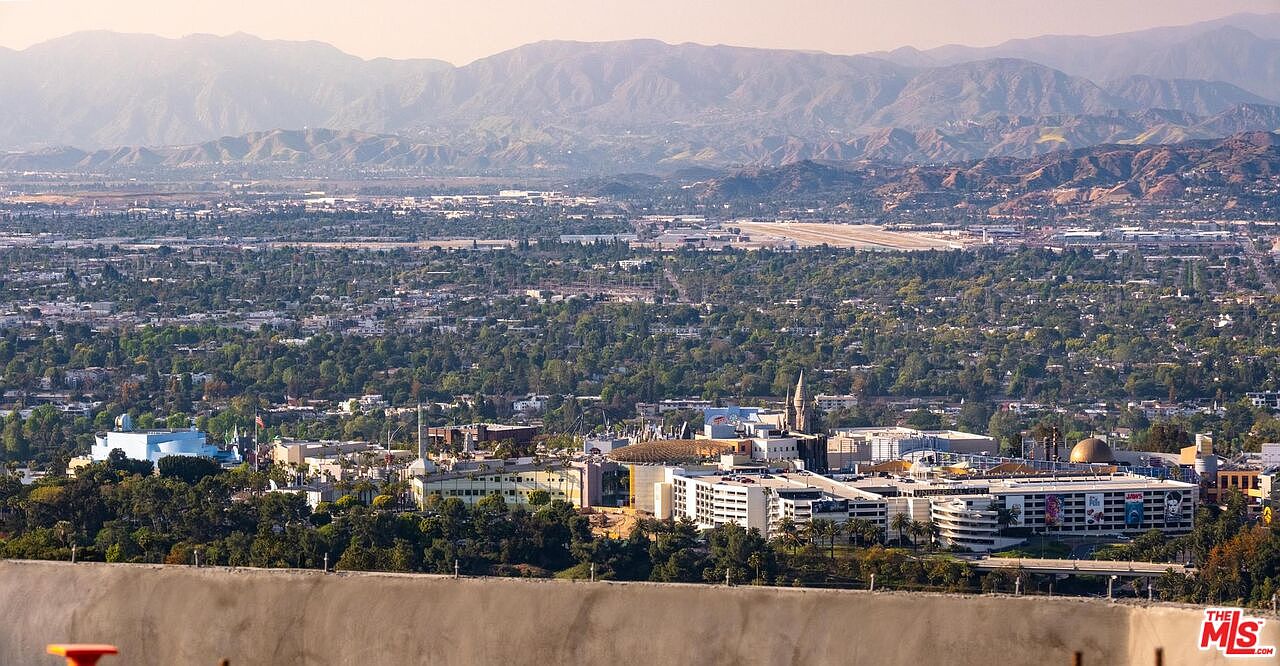 This aerial view showcases a sprawling cityscape nestled against a backdrop of majestic mountains. The foreground features a cluster of buildings with diverse architectural styles, surrounded by lush greenery. The image captures a sense of urban sophistication blended with natural beauty, ideal for highlighting the location's appeal.