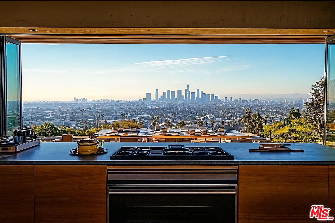 This image showcases a modern kitchen with a stunning panoramic view of a cityscape. The kitchen features sleek wooden cabinetry, a black stovetop, and a built-in oven. The expansive window seamlessly blends the indoor and outdoor spaces, creating a luxurious and inviting atmosphere.