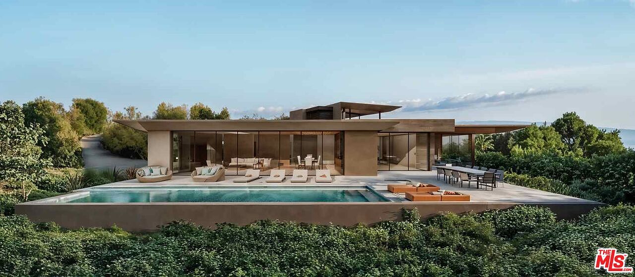 This image showcases a modern luxury home with a stunning pool and outdoor living space. The architecture features clean lines, large glass windows, and a flat roof, blending seamlessly with the natural surroundings. The pool is surrounded by a spacious patio with lounge chairs and outdoor dining furniture, perfect for entertaining and relaxation.