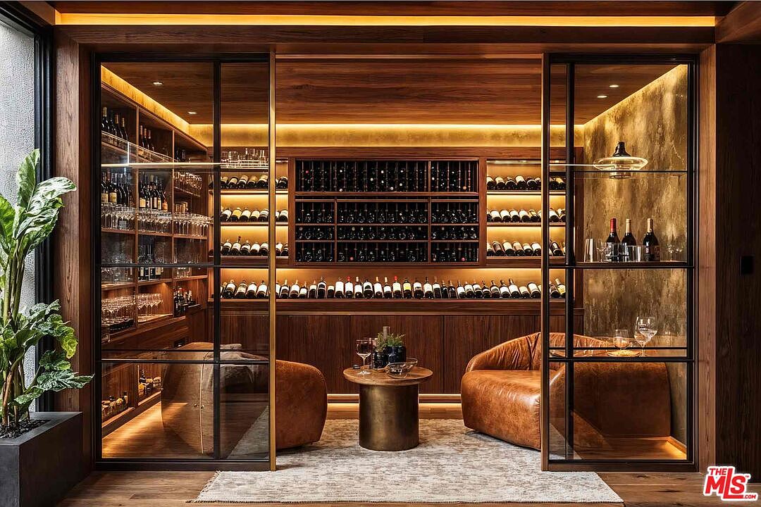 This image showcases a luxurious wine cellar with a sophisticated design. The cellar features extensive wooden shelving filled with wine bottles, illuminated by warm lighting that highlights the rich wood tones. Two leather armchairs and a small table create a cozy tasting area, enhancing the cellar's appeal as a refined space for wine enthusiasts.