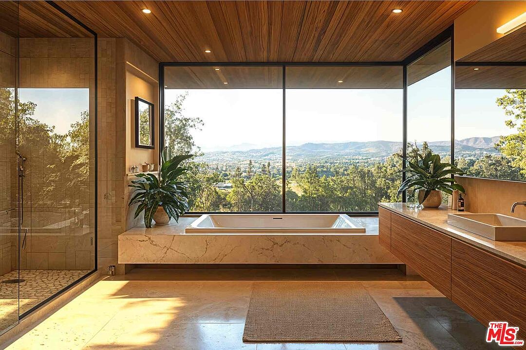 This is a luxurious primary bathroom featuring a modern design with natural elements. A large soaking tub is positioned in front of a wide window offering scenic views of the landscape. The bathroom also includes a glass-enclosed shower and a sleek vanity with a vessel sink, all contributing to a spa-like atmosphere.
