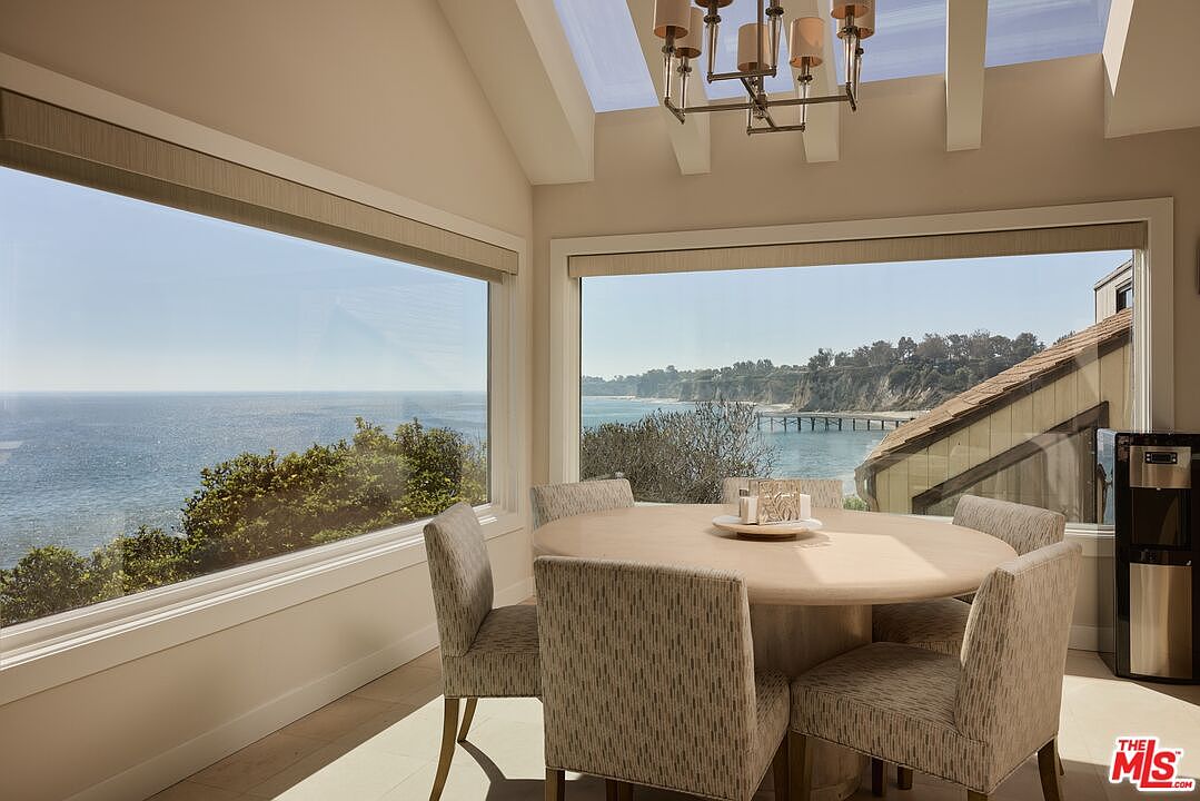 This dining room features a round table with six chairs, positioned in front of large windows that offer stunning ocean views. A modern chandelier hangs above the table, and the room is filled with natural light. The overall impression is one of elegance and tranquility, perfect for enjoying meals with a view.