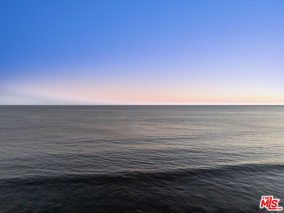 The image showcases a serene ocean view under a clear blue sky transitioning to a soft gradient near the horizon. The water is calm with gentle waves, reflecting the colors of the sky. The overall impression is peaceful and expansive, emphasizing the property's proximity to the ocean.