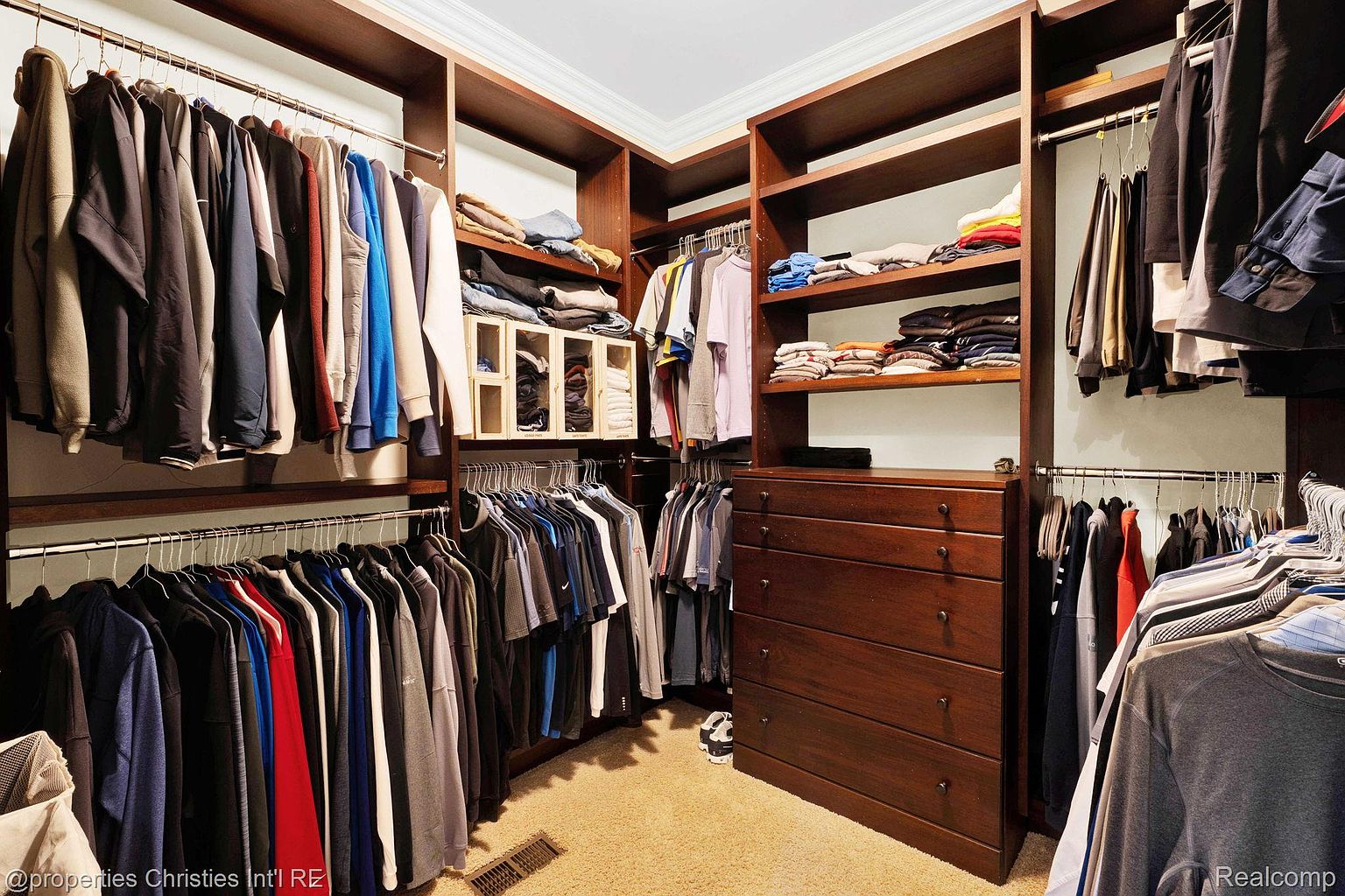This is a well-organized walk-in closet featuring dark wood shelving and drawers. Clothes are neatly hung on rods, and folded items are arranged on shelves. The closet offers ample storage space and a luxurious feel, making it a desirable feature for potential buyers.