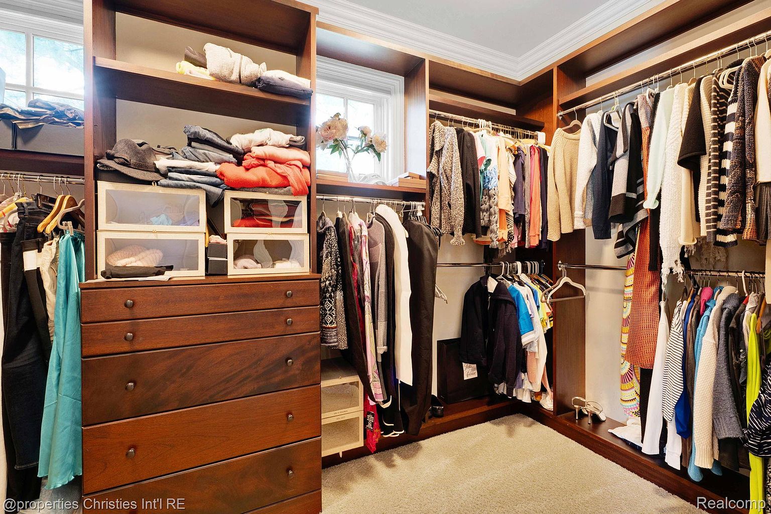 This is a well-organized walk-in closet with custom wood shelving and drawers. The closet features hanging rods for clothes, open shelves for folded items, and clear storage boxes. The overall impression is one of luxury and efficient use of space, perfect for showcasing storage solutions in a real estate listing.