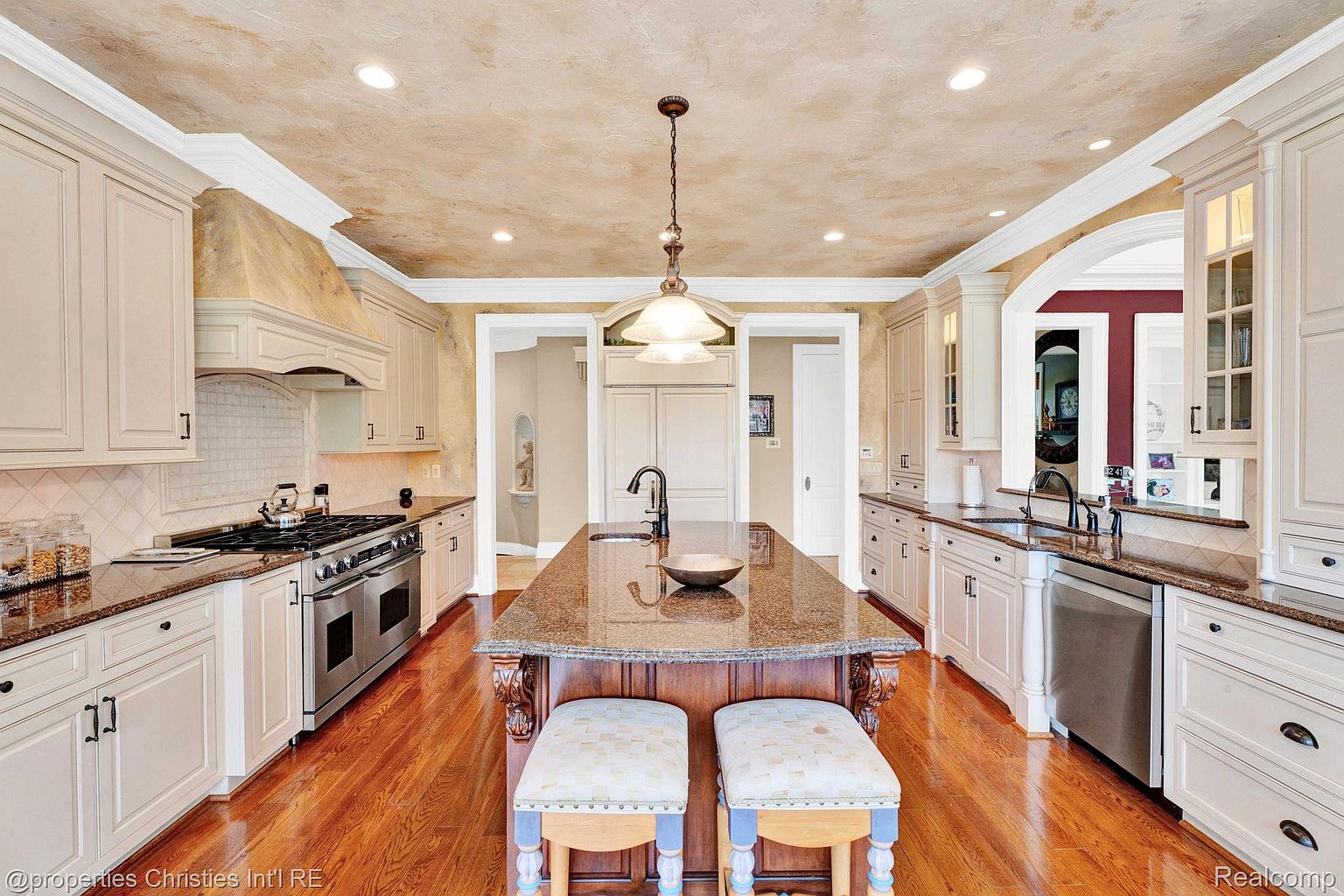 This is a well-lit kitchen featuring custom cabinetry, granite countertops, and stainless steel appliances. A large island with seating provides a central gathering point, while the hardwood floors add warmth to the space. The kitchen's design blends functionality with a touch of elegance, making it a focal point of the home.