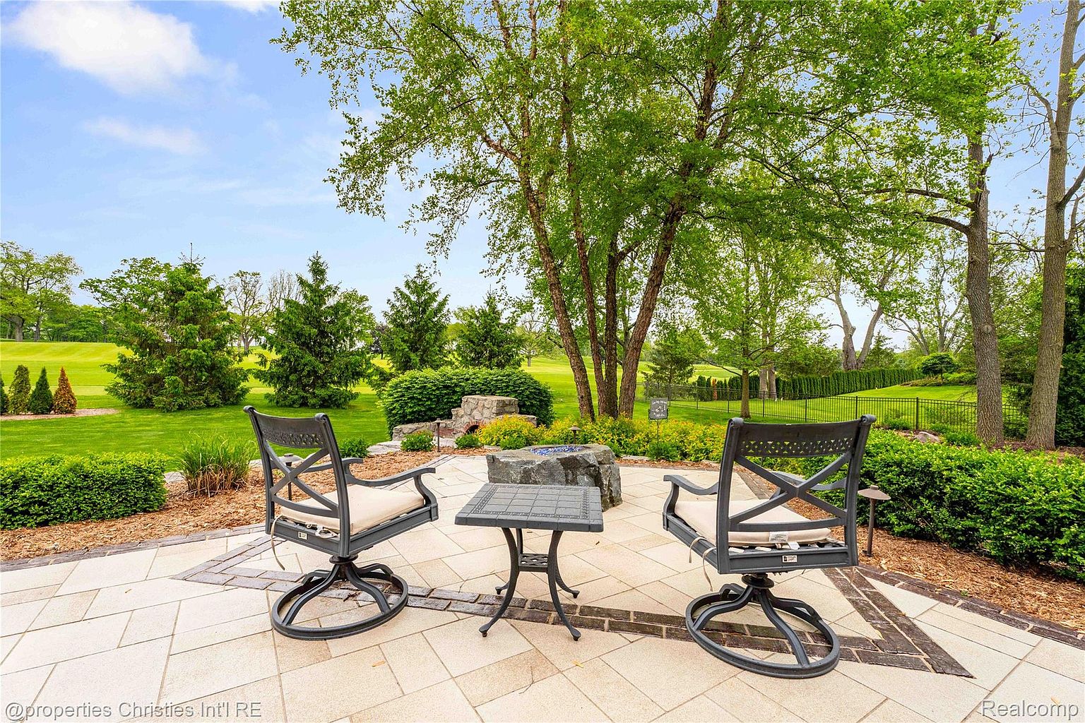 This image showcases a beautifully designed patio area, perfect for outdoor relaxation and entertaining. The patio features elegant stone paving, complemented by comfortable seating around a modern fire pit. Lush landscaping surrounds the space, creating a serene and private backyard oasis.