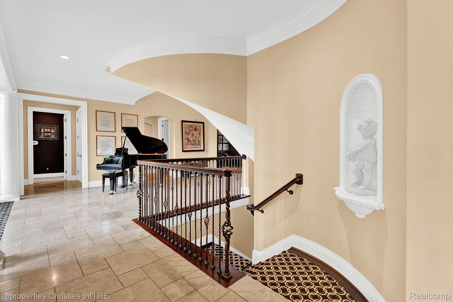 This interior shot showcases an elegant hallway and staircase. A grand piano sits adjacent to the hallway, adding a touch of sophistication. The staircase features ornate wrought iron railings and a decorative niche with a statue, contributing to the home's luxurious ambiance.