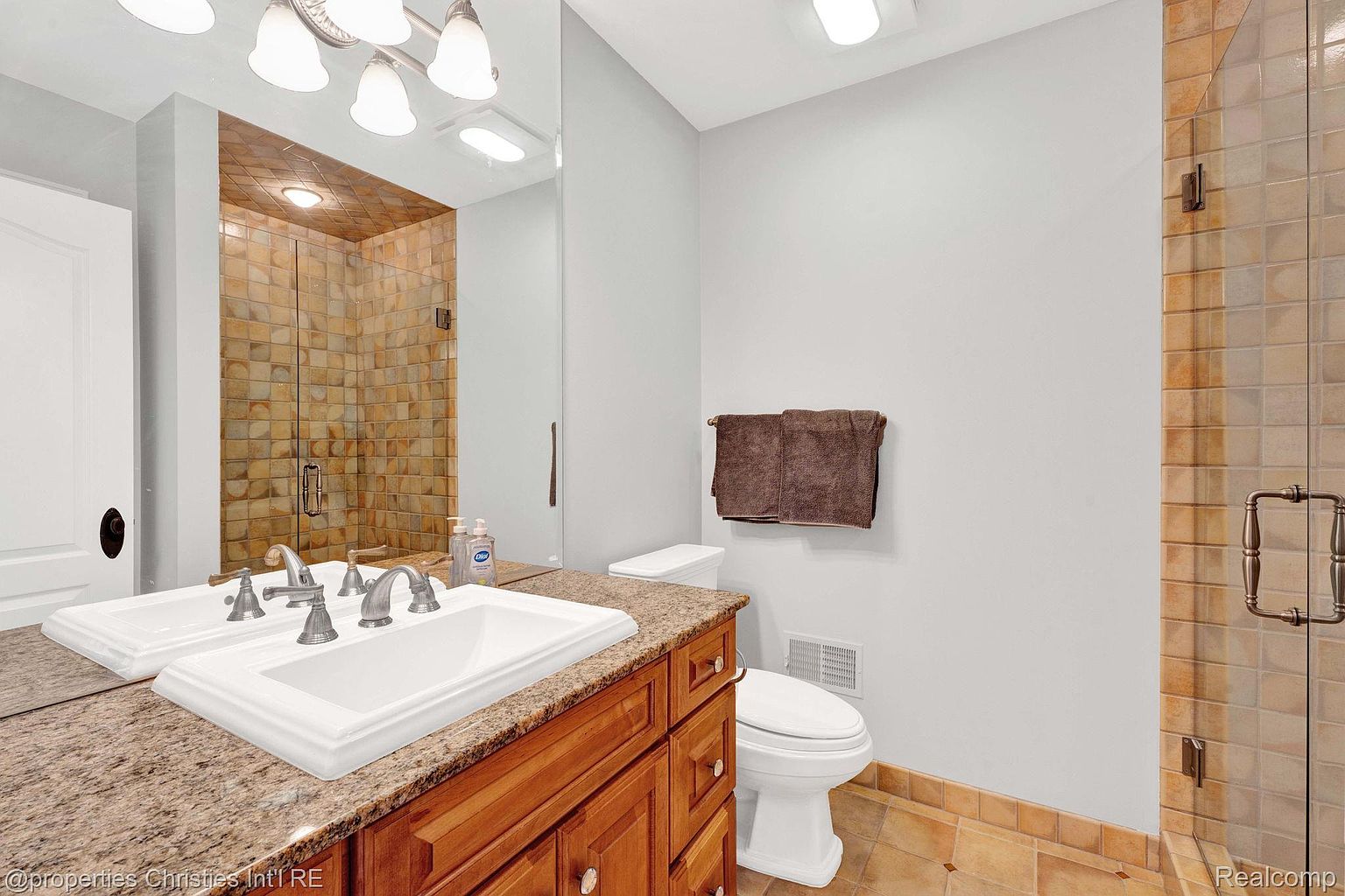 This is a primary bathroom featuring a double sink vanity with a granite countertop and wooden cabinets. A large mirror reflects the vanity and a tiled shower. The bathroom also includes a toilet and a separate tiled shower stall, creating a functional and luxurious space.
