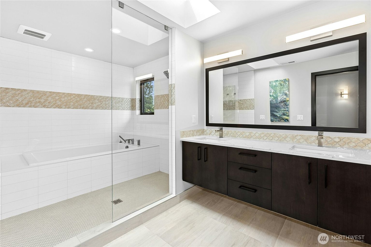 This modern primary bathroom features a sleek, double-vanity with dark wood cabinetry and a large, framed mirror. A spacious walk-in shower with a glass enclosure is integrated with a soaking tub, accented by a decorative tile backsplash. The room is bright and airy, highlighted by neutral tones and clean, contemporary finishes.