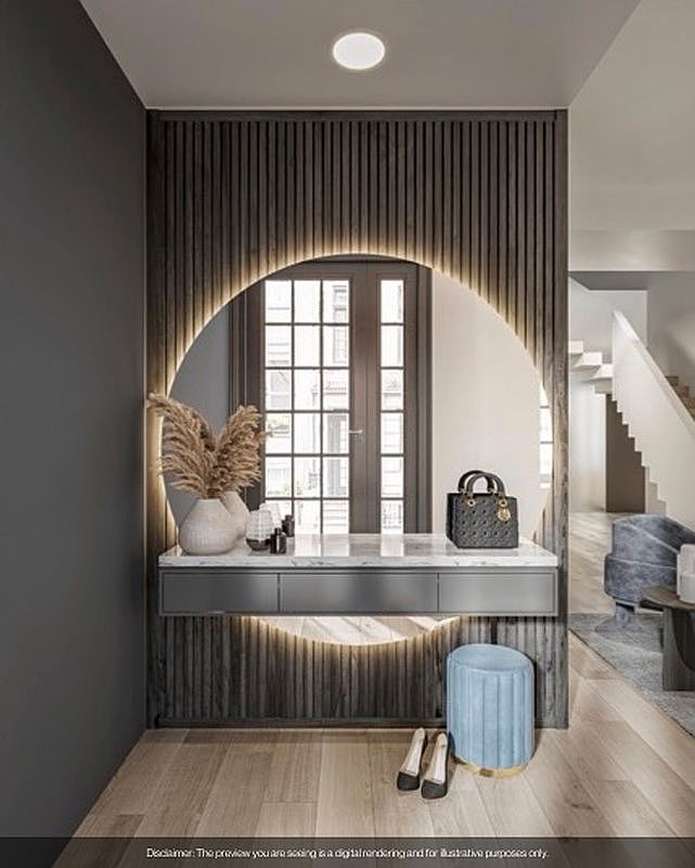 The image showcases a stylish entryway or hallway featuring a vanity area with a circular mirror illuminated by soft lighting. The vanity is complemented by a light blue stool and a pair of shoes placed neatly on the wooden floor. In the background, a glimpse of a staircase and a seating area adds depth and suggests a well-designed interior space.