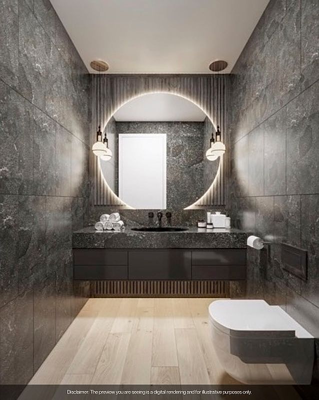 This is a modern bathroom featuring dark gray stone tile walls and light wood flooring. A floating vanity with a dark countertop and integrated sink is illuminated by a circular LED mirror with sconces. A wall-mounted toilet completes the minimalist design, creating a sleek and contemporary space.
