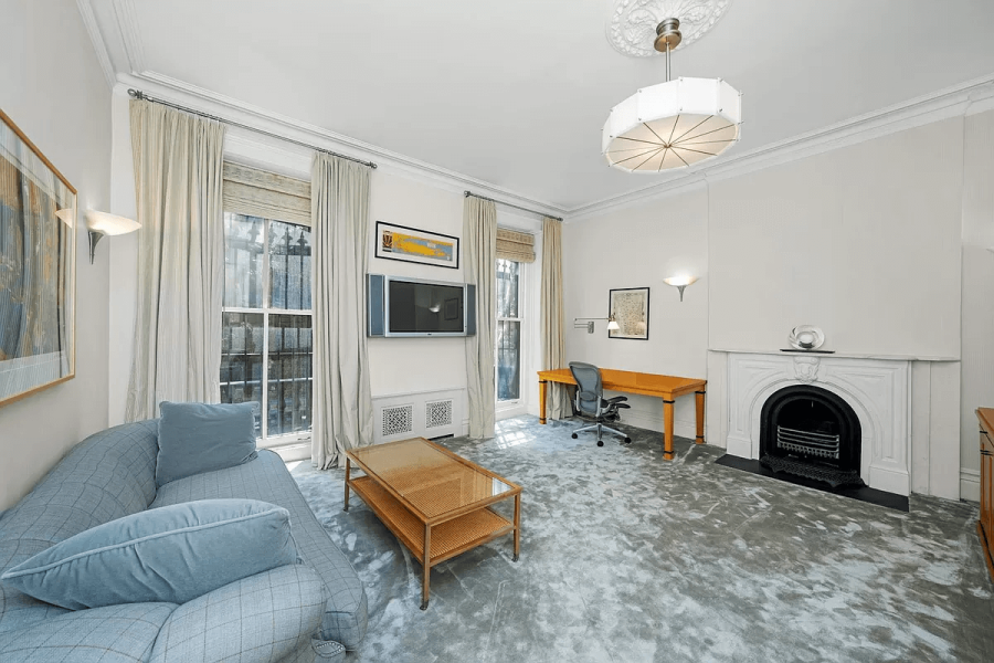 This living room features a blend of traditional and contemporary styles. A blue sofa anchors the space, while a fireplace and large windows offer classic charm. The room also incorporates a workspace with a desk, creating a functional and inviting atmosphere.