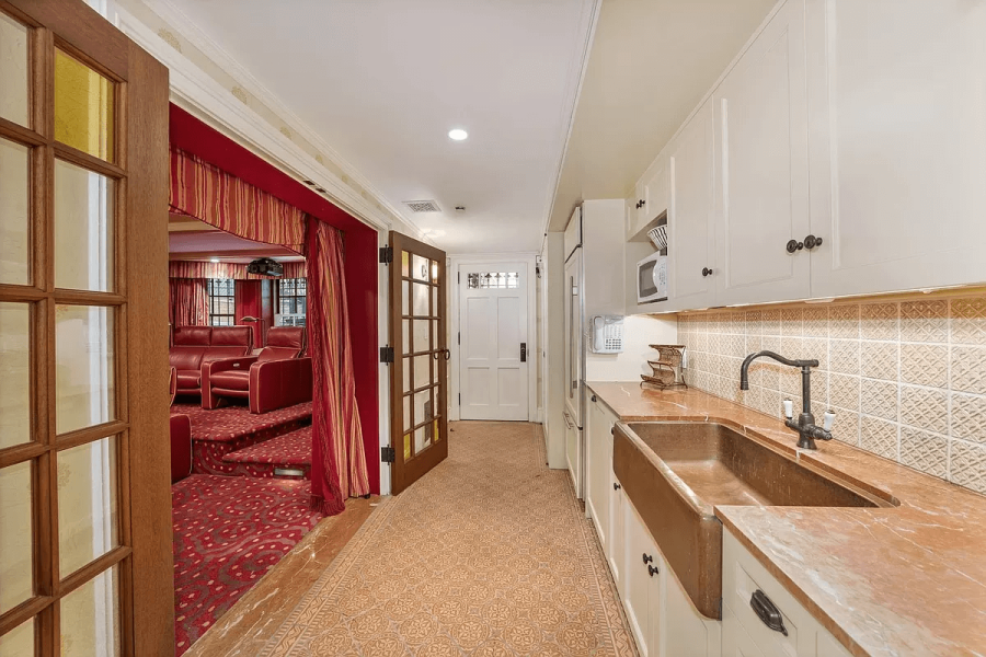 This interior shot features a kitchen area complete with white cabinetry and copper countertops. The space also includes a unique copper farmhouse sink. A hallway leads to a theater room, visible through an open doorway, offering a glimpse of tiered seating and red decor.