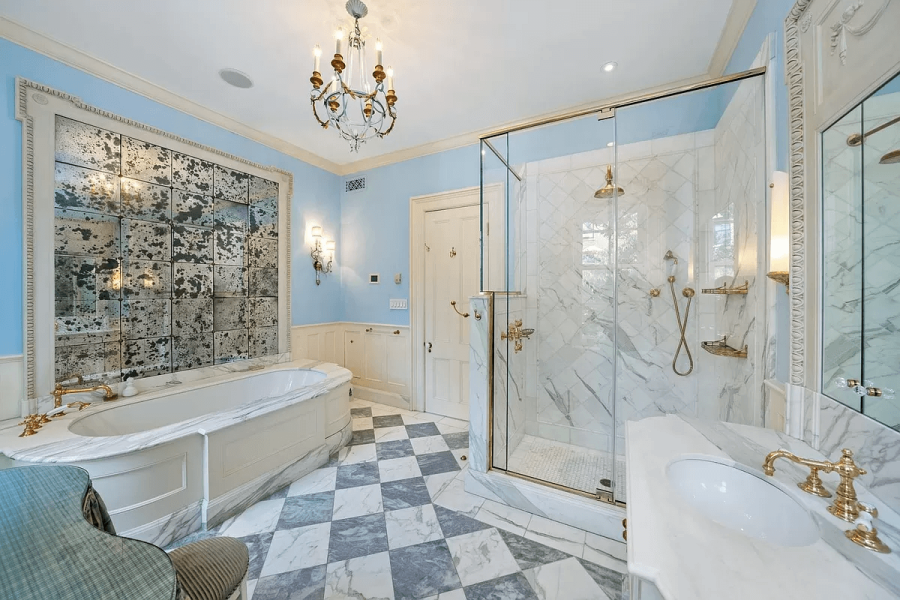 This is a luxurious primary bathroom featuring a freestanding tub with antique mirror backsplash, a glass-enclosed shower, and a marble countertop vanity. The color scheme is light blue and white, accented with gold fixtures. The overall style is elegant and sophisticated.