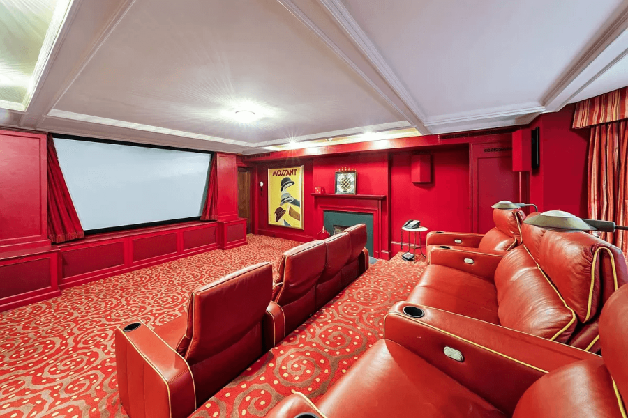 This is an interior view of a home theater. The room features red walls, red leather theater seating with cup holders, and a large screen. A colorful movie poster and a fireplace add to the ambiance.