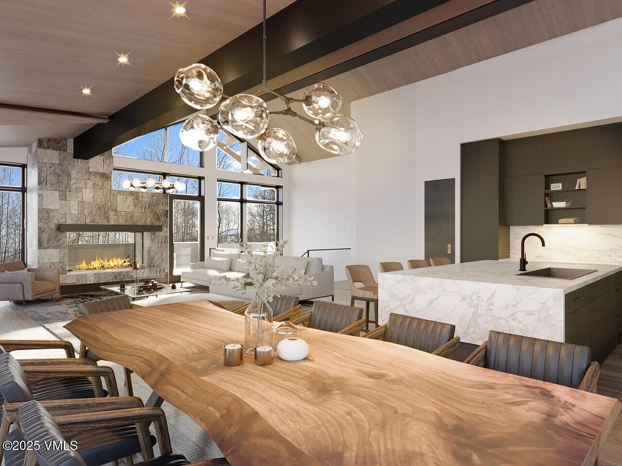 This interior shot showcases a modern dining room with a large, natural-edge wooden table as the centerpiece, surrounded by stylish chairs. A contemporary bubble chandelier hangs above the table, adding a touch of elegance. The open-concept design flows into a living area with a stone fireplace and a kitchen with marble countertops, creating a cohesive and luxurious living space.