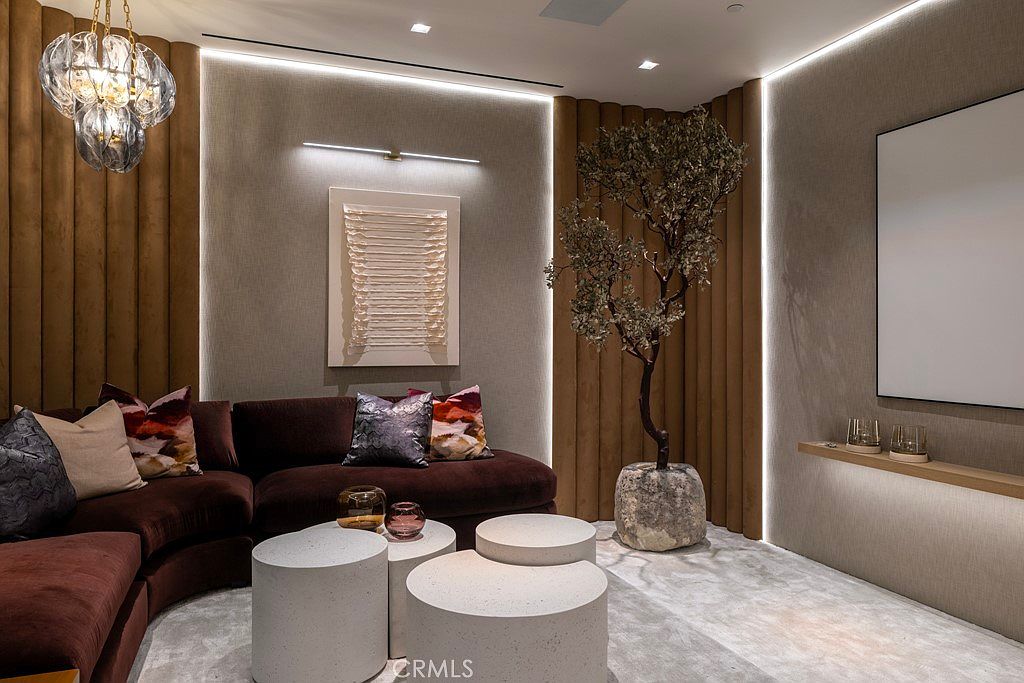 This is an interior shot of a modern living room featuring a brown sectional sofa adorned with decorative pillows. The room is decorated with a unique art piece, a decorative tree, and a set of modern, cylindrical coffee tables. The lighting is soft and ambient, creating a warm and inviting atmosphere.