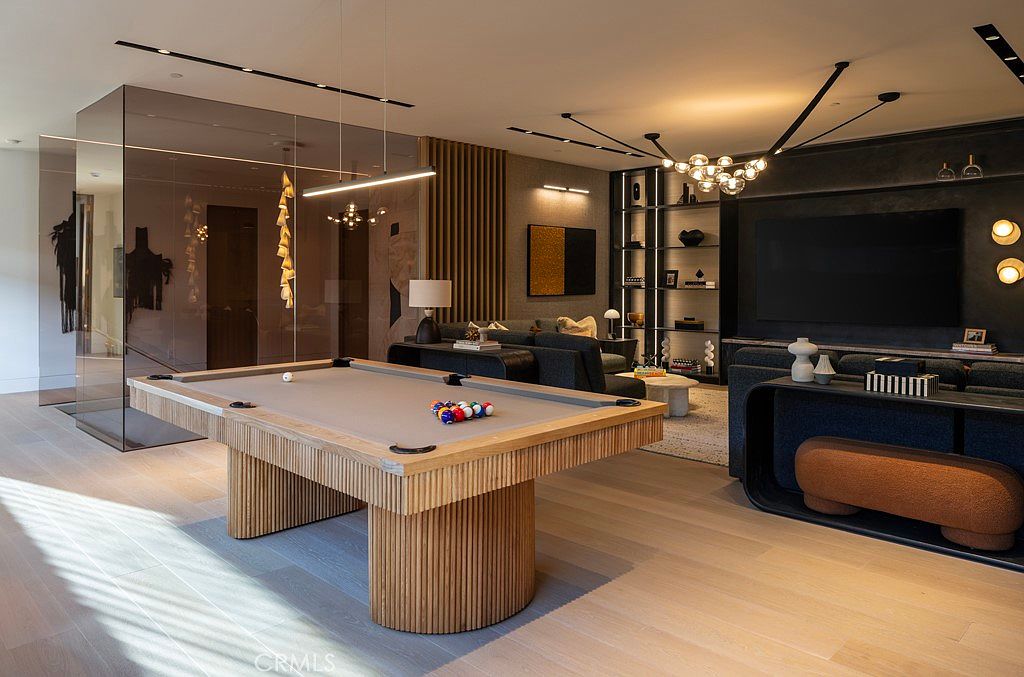 This interior shot showcases a modern living room with a pool table as a central feature. The room is stylishly decorated with a large television, built-in shelving, and contemporary lighting fixtures. The color palette is neutral with wood accents, creating a sophisticated and inviting atmosphere.