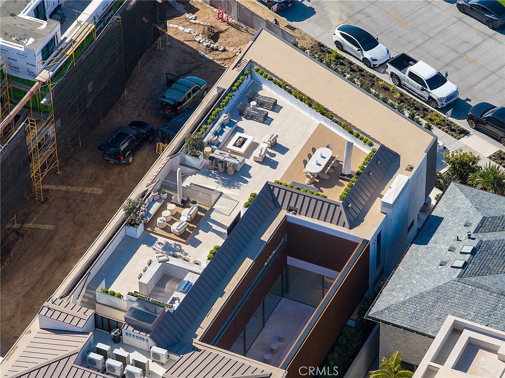 This aerial shot showcases a modern luxury home with multiple rooftop terraces. The terraces feature outdoor living spaces with seating areas, dining tables, and landscaping. The property also includes a unique courtyard design and is surrounded by other residential buildings and street parking.
