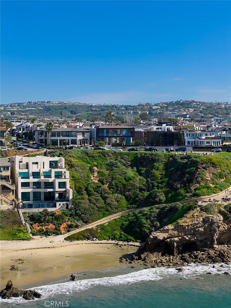 This image showcases a coastal property with a multi-story building situated on a cliff overlooking the ocean. The architecture features modern design elements, including large windows and clean lines. Lush greenery covers the hillside, adding to the property's appeal and creating a sense of privacy. The perspective is a wide shot, capturing the building, the landscape, and the ocean in a single frame.