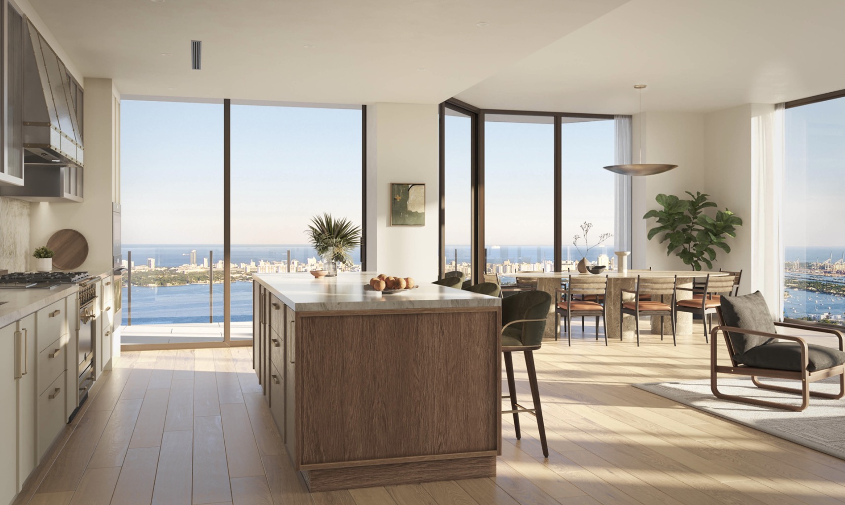 This is a bright and modern kitchen with an open floor plan, featuring a large island with seating, sleek cabinetry, and high-end appliances. Expansive windows offer stunning ocean and city views, enhancing the luxurious feel of the space. The hardwood flooring and contemporary furnishings create a warm and inviting atmosphere.